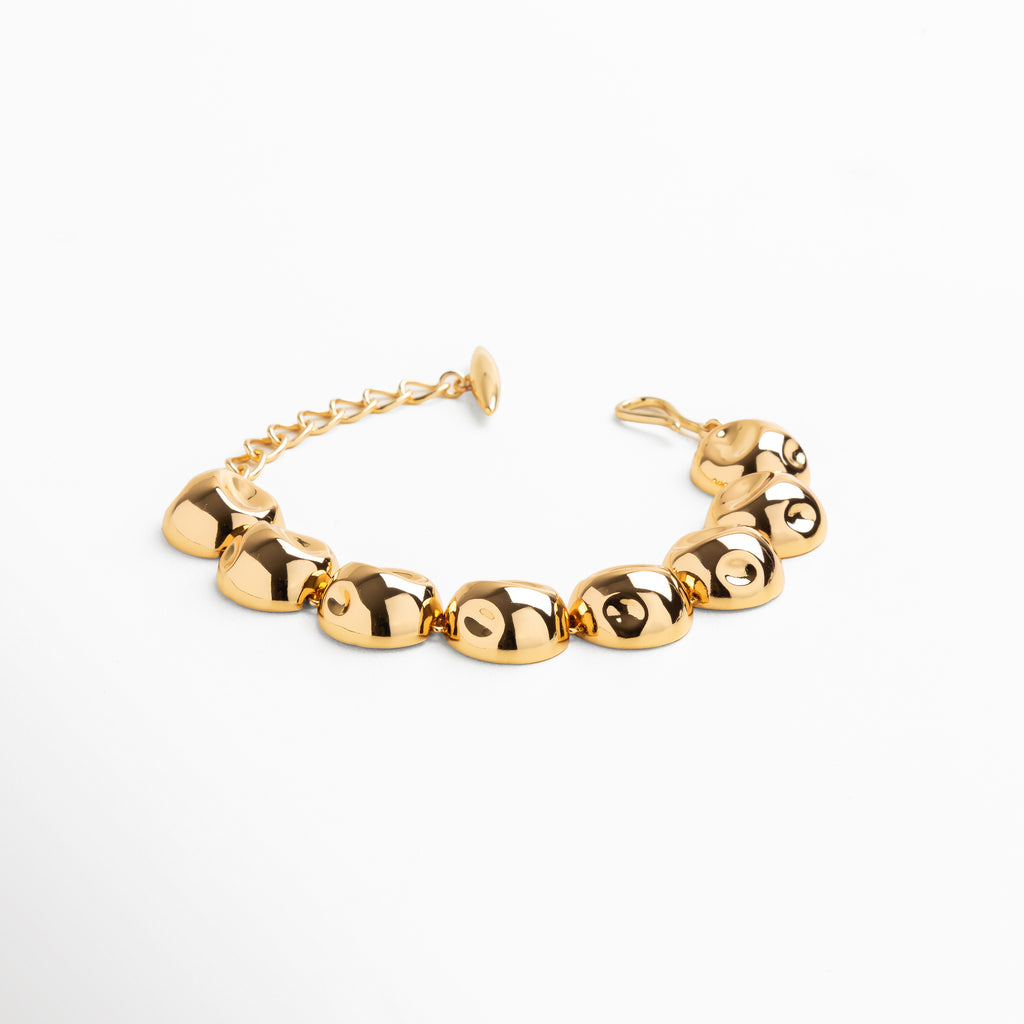 Primer plano de esferas doradas pulidas con reflejo brillante, Detalle de acabado espejo en cuentas metálicas doradas, Conexión uniforme entre bolitas en pulsera dorada, Superficie lisa y pulida de cada esfera, Textura brillante y continua en pulsera de cuentas doradas