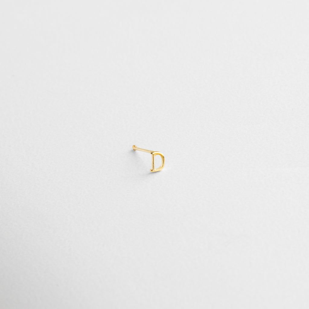 Engarce limpio en forma de letra, Contorno nítido y proporciones delicadas, Base de Plata .925 con recubrimiento dorado, Reflejo dorado sobre fondo neutro, Grosor sutil con apariencia elegante