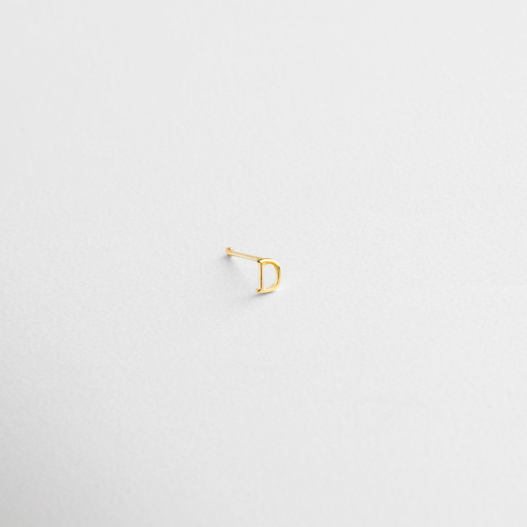 Engarce limpio en forma de letra, Contorno nítido y proporciones delicadas, Base de Plata .925 con recubrimiento dorado, Reflejo dorado sobre fondo neutro, Grosor sutil con apariencia elegante