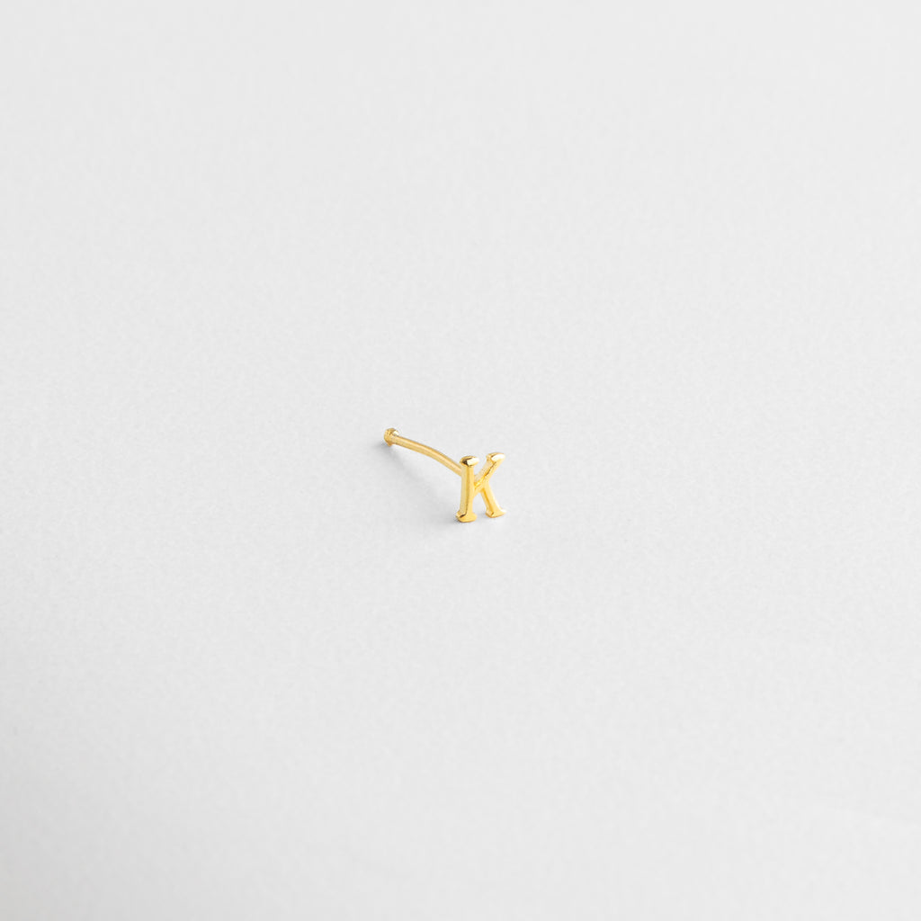 Acabado brillante en forma de inicial, Detalle del grabado limpio en dorado, Pulido fino sobre la superficie de la letra, Letra en joyería mini con brillo sutil, Zoom al trazo definido del diseño