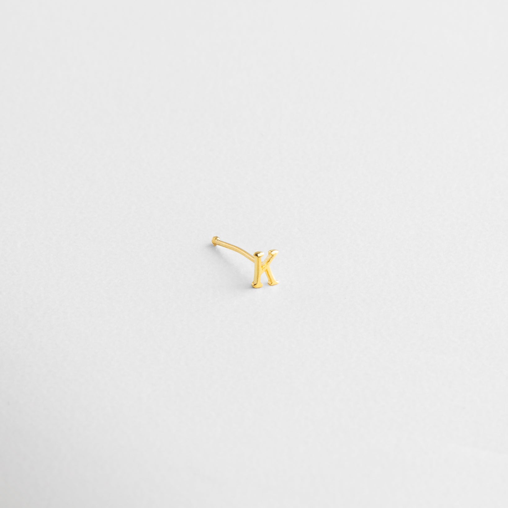 Acabado brillante en forma de inicial, Detalle del grabado limpio en dorado, Pulido fino sobre la superficie de la letra, Letra en joyería mini con brillo sutil, Zoom al trazo definido del diseño