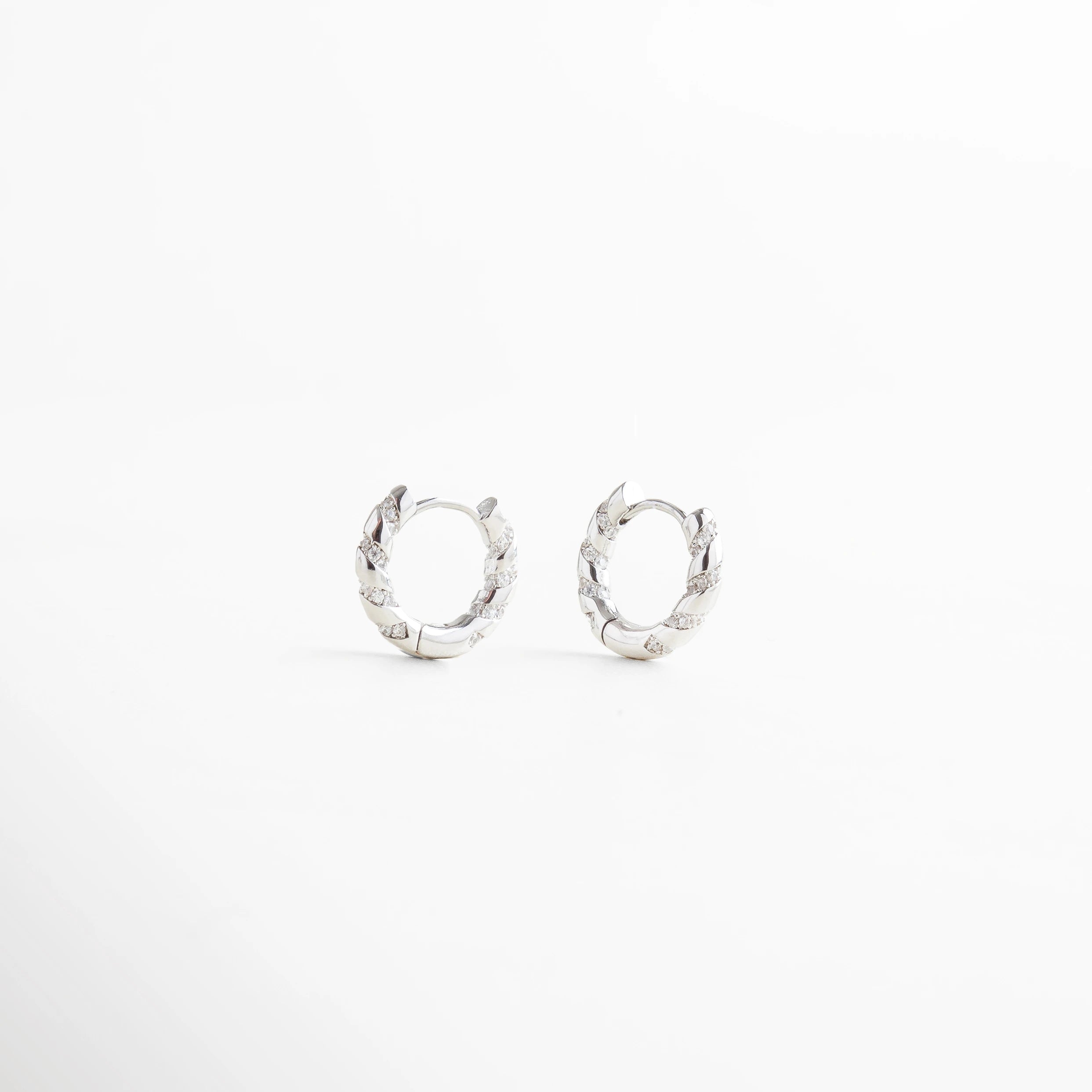 Aretes de aro plateados pequeños con diseño trenzado, estilo moderno y elegante, Arracadas plateadas con textura entrelazada, joyería minimalista y sofisticada.