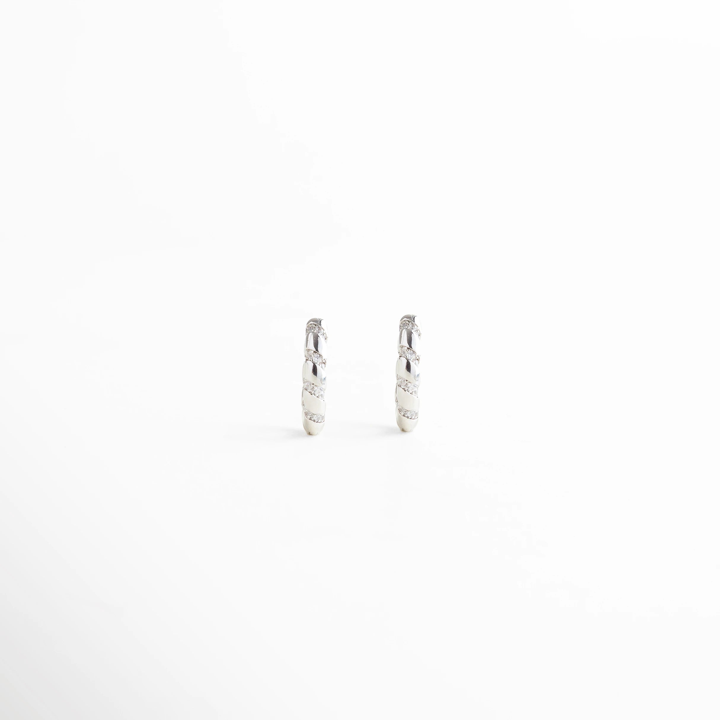 Aros plateados pequeños con acabado trenzado, diseño clásico y elegante, Aretes plateados estilo trenza vistos de frente, accesorios atemporales y versátiles.