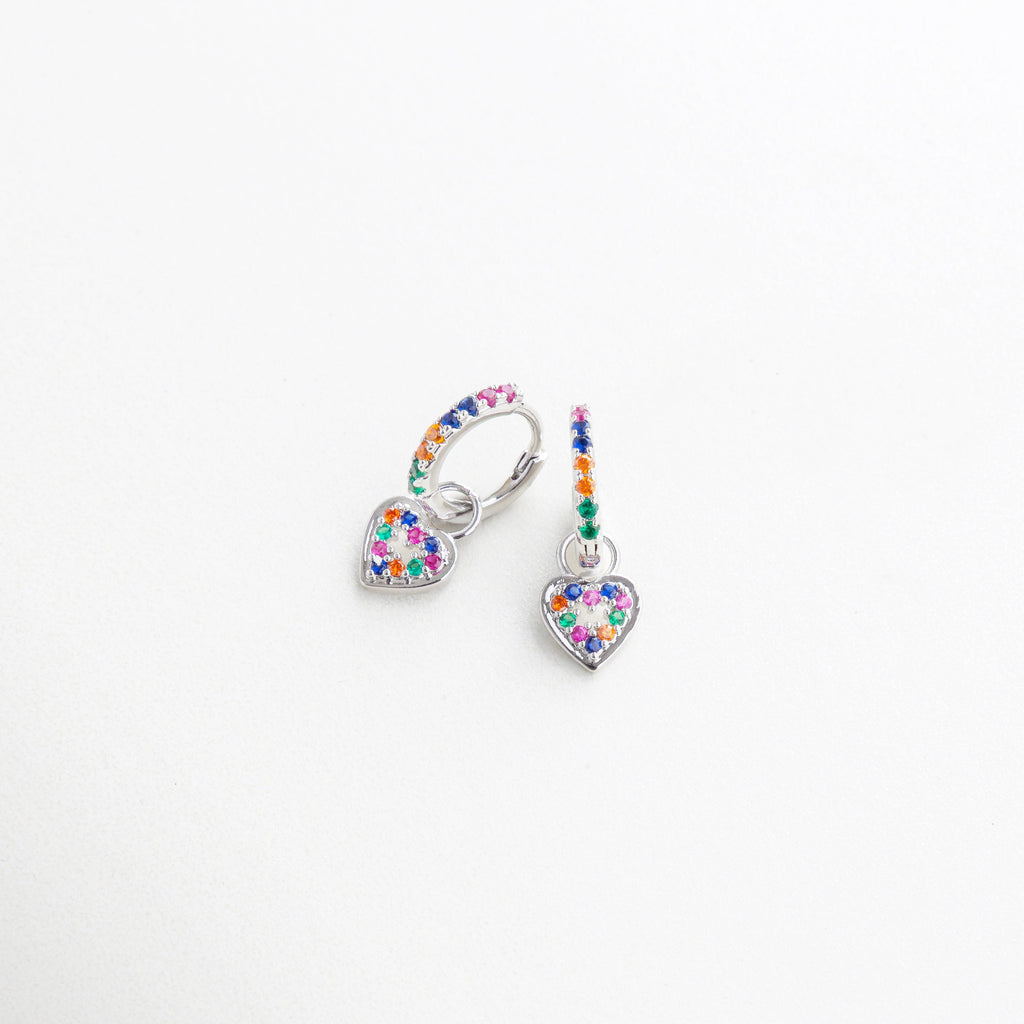 Aretes plateados con corazón colgante vistos de perfil, Diseño curvado con charm colorido en perspectiva, Arracadas en ángulo con piedras de colores, Pendientes plateados con detalle romántico