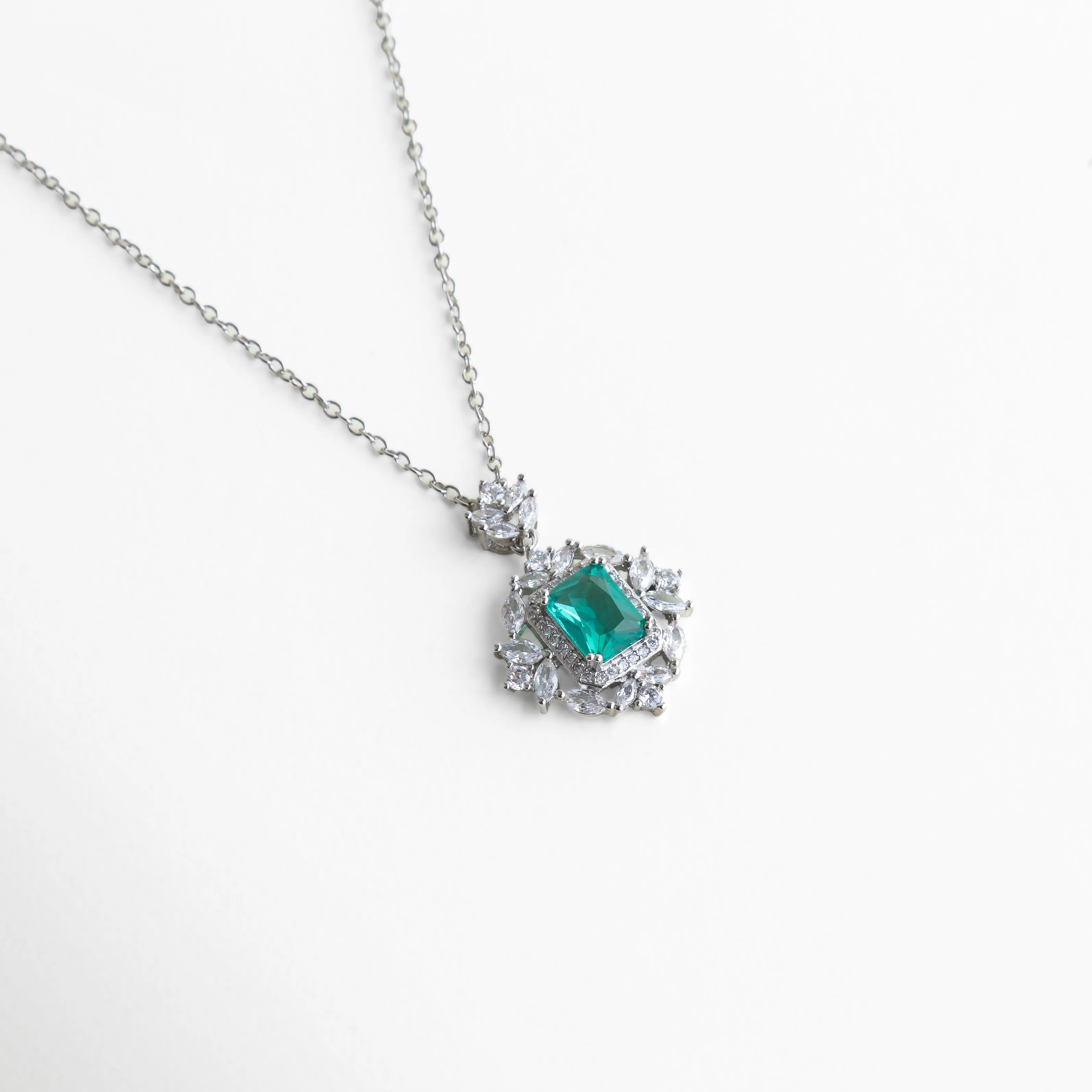 collar plateado con dije verde esmeralda visto en diagonal sobre fondo blanco