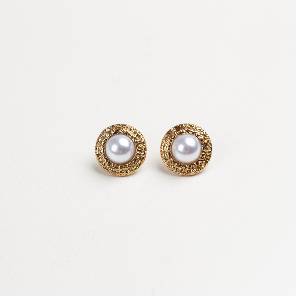 Aretes redondos con borde dorado texturizado y una perla en el centro, que combinan elegancia clásica con un diseño moderno y detallado, ideales para elevar cualquier atuendo con un toque sofisticado.