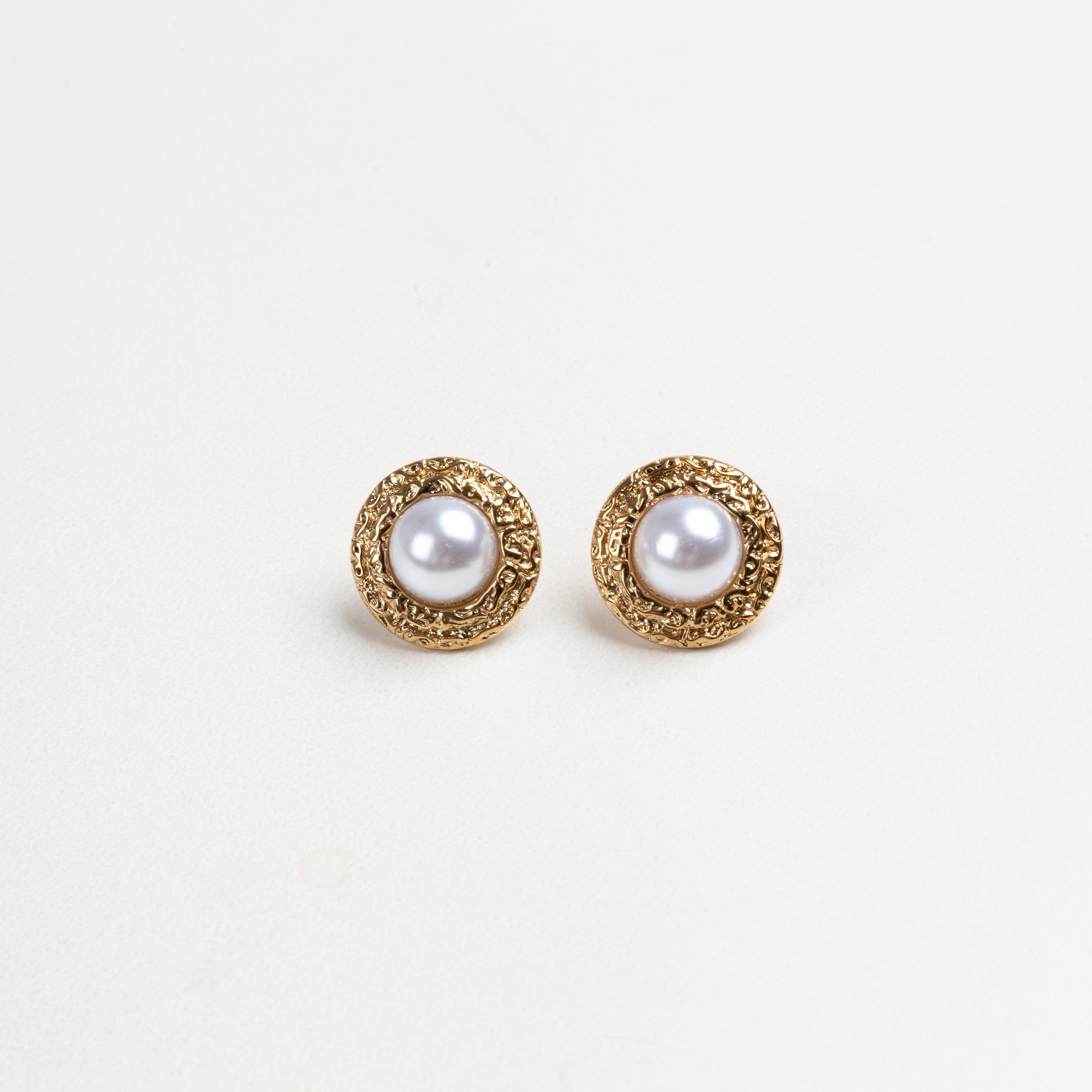 Aretes redondos con borde dorado texturizado y una perla en el centro, que combinan elegancia clásica con un diseño moderno y detallado, ideales para elevar cualquier atuendo con un toque sofisticado.