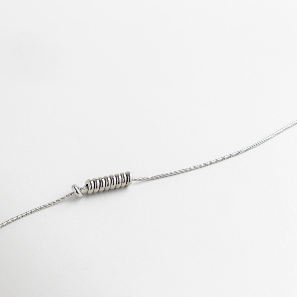 Primer plano de cadena y dije minimalista con acabado plata, pequeños detalles circulares que aportan textura y sofisticación, pieza ideal para combinar con otras joyas o usar sola con elegancia discreta