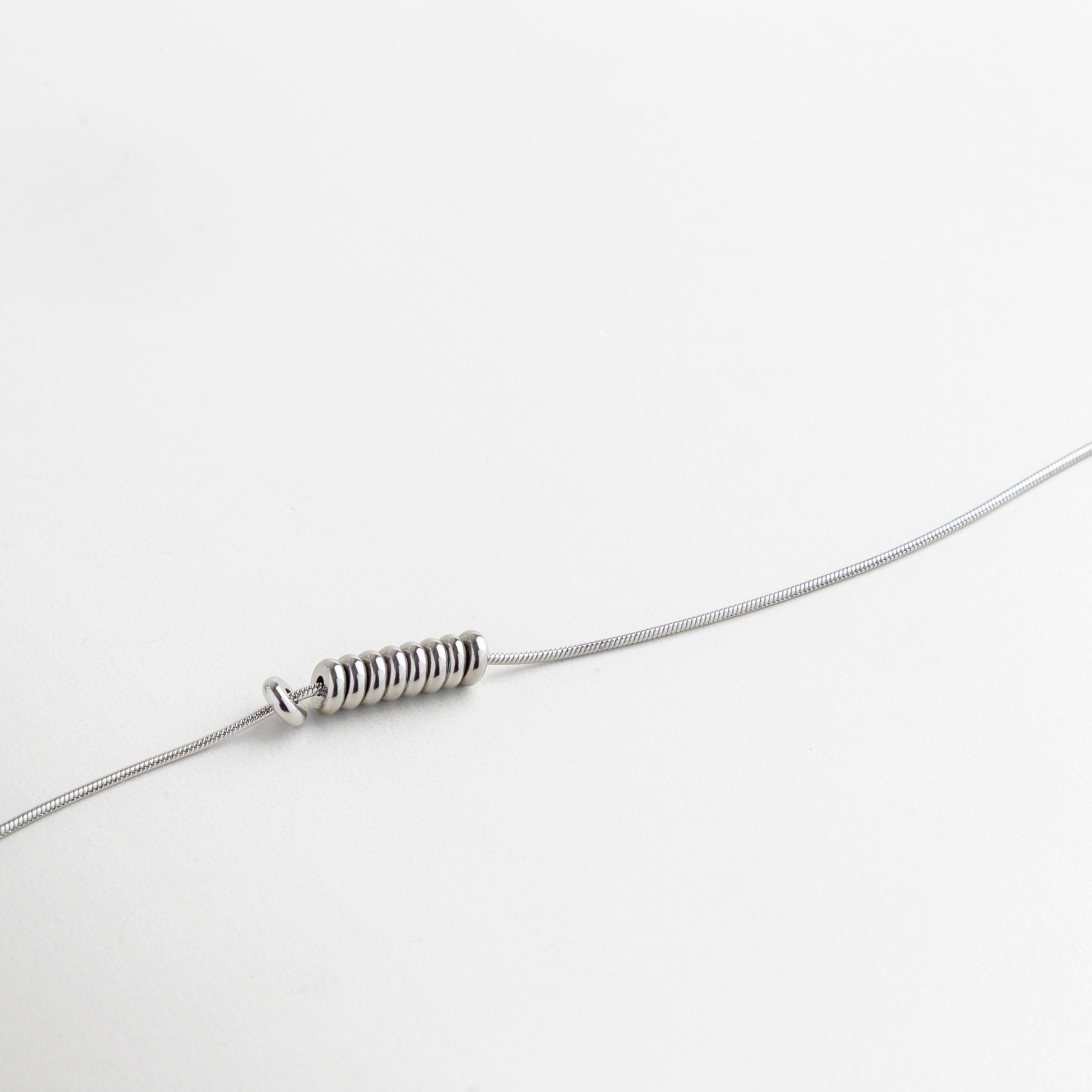 Primer plano de cadena y dije minimalista con acabado plata, pequeños detalles circulares que aportan textura y sofisticación, pieza ideal para combinar con otras joyas o usar sola con elegancia discreta