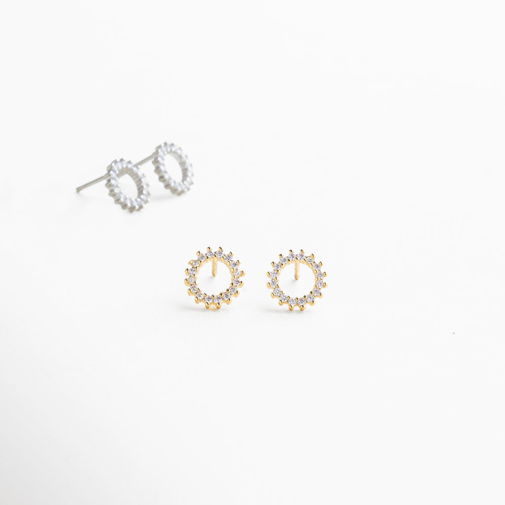 detalle de zirconias cúbicas en aretes dorados, incrustaciones brillantes sobre base dorada pulida, textura lisa y brillante del arillo dorado, borde redondeado en aretes con zirconias, enfoque en piedras transparentes sobre acabado oro 18K