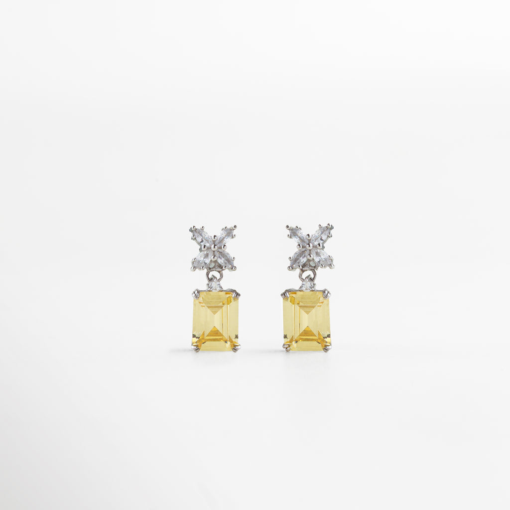 Aretes plateados con piedra amarilla cuadrada al centro, vistos de frente sobre fondo neutro. Vista frontal de aretes elegantes en tono plateado, con piedra amarilla brillante en corte cuadrado. Aretes rectangulares plateados con centro amarillo, estilo refinado y sofisticado. Primer plano frontal de par de aretes plateados con piedra amarilla en diseño clásico y elegante.Aretes plateados con incrustación cuadrada amarilla, vistos de frente con acabado brillante.