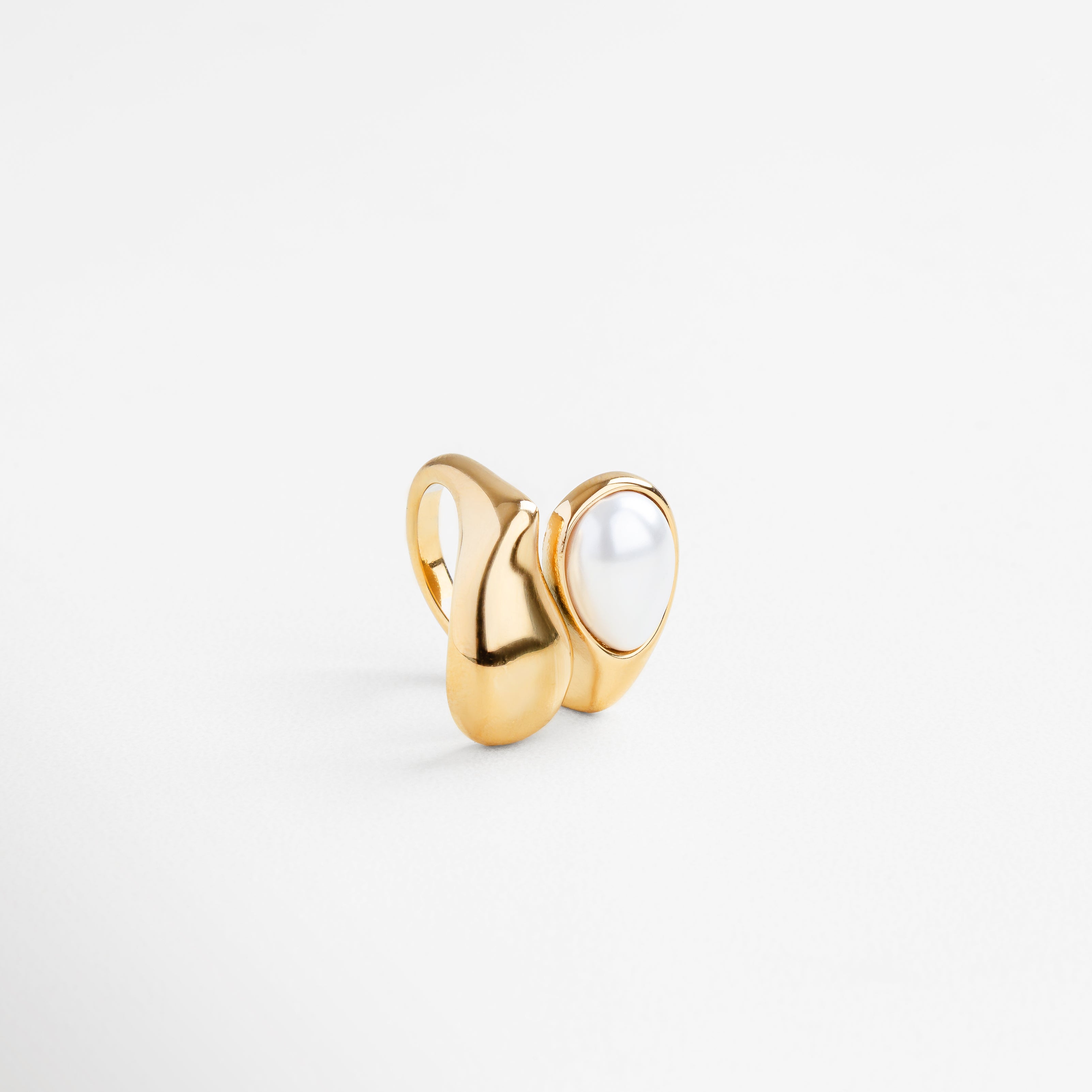 Detalle de la perla blanca en anillo dorado, Textura pulida del anillo Akari con perla central, Incrustación de perla en diseño dorado fluido, Acabado brillante y curvo con perla como protagonista