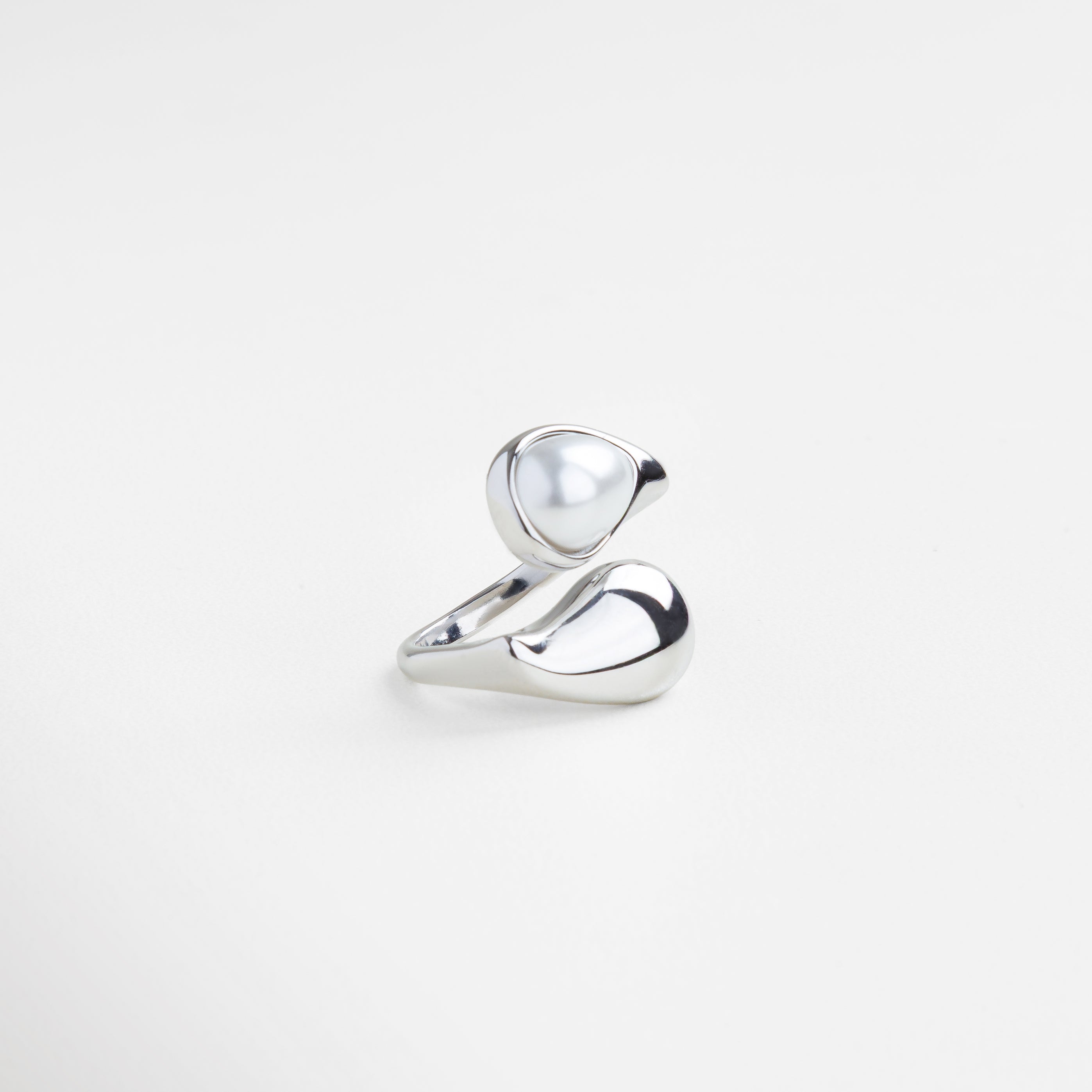 Anillo con perla en forma ondulada desde ángulo lateral, Perfil escultórico del anillo plateado con perla, Diseño envolvente en plateado con perla central, Curvas modernas en plata con perla elevada