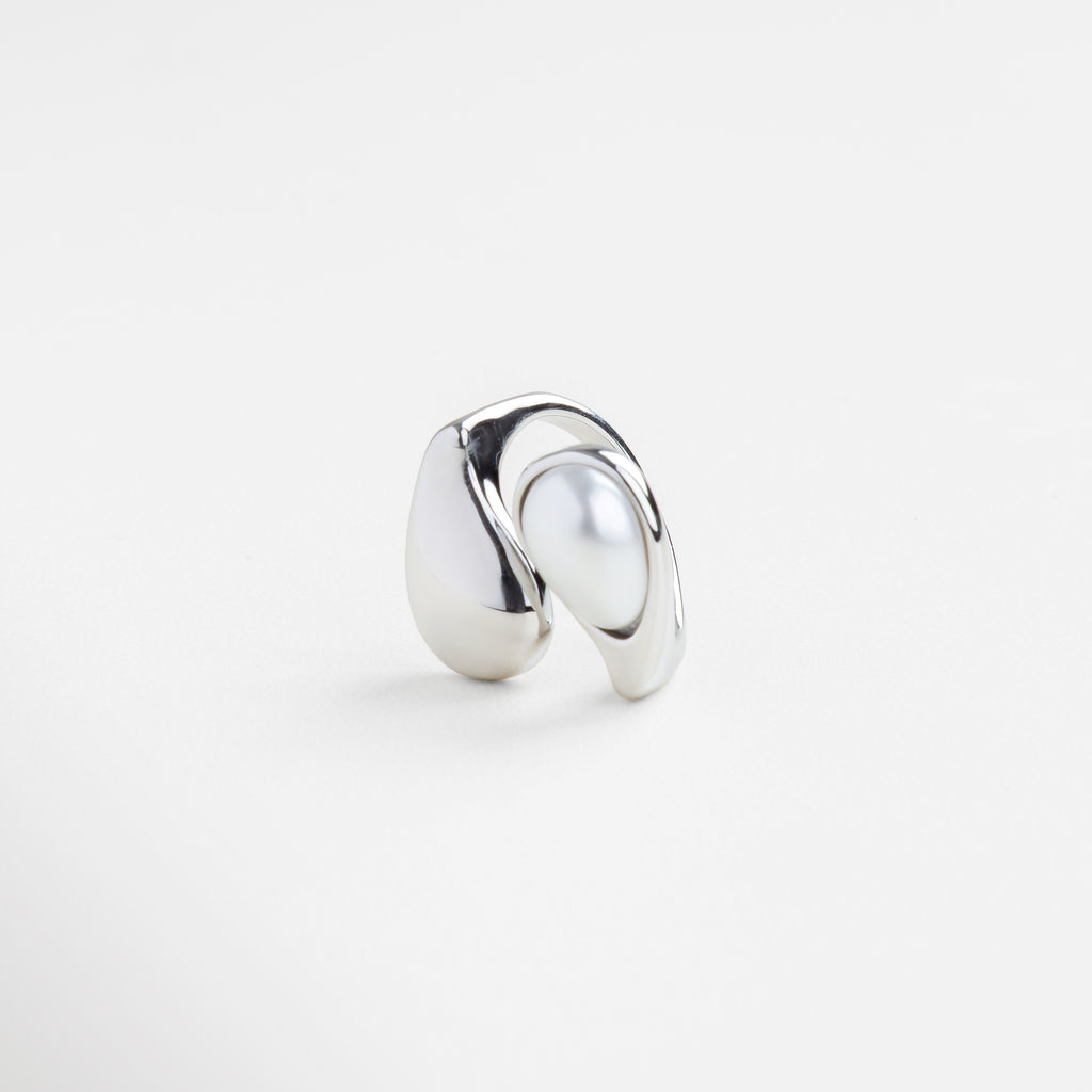 Detalle de perla blanca sobre anillo plateado brillante, Textura pulida del anillo Akari en acabado plateado, Inserción de perla en estructura curva de plata, Brillo metálico y perla en diseño minimalista