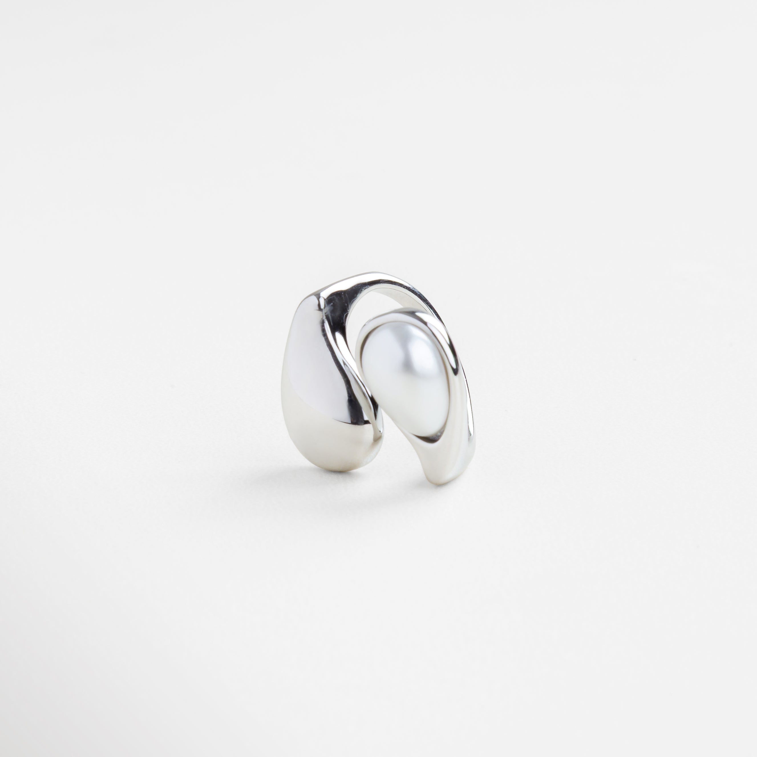 Detalle de perla blanca sobre anillo plateado brillante, Textura pulida del anillo Akari en acabado plateado, Inserción de perla en estructura curva de plata, Brillo metálico y perla en diseño minimalista