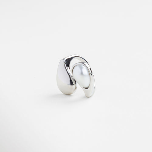Detalle de perla blanca sobre anillo plateado brillante, Textura pulida del anillo Akari en acabado plateado, Inserción de perla en estructura curva de plata, Brillo metálico y perla en diseño minimalista