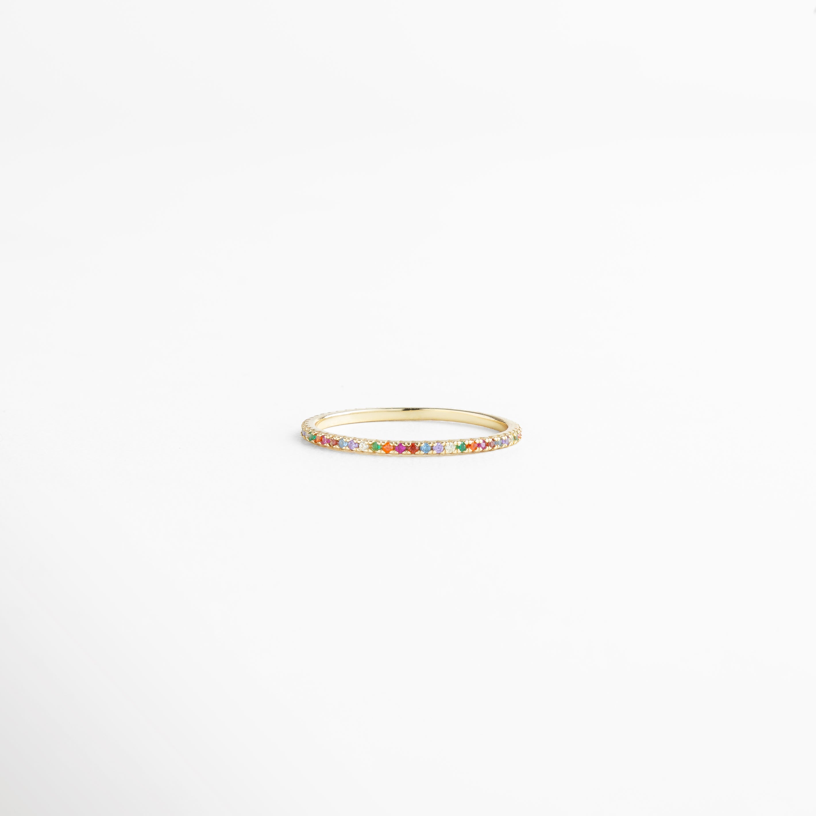 Anillo de plata Ley 925 con recubrimiento enchapado en oro 18K, incrustaciones de zirconias multicolor en diseño delicado y elegante, pieza fina de joyería minimalista mostrada en vista horizontal sobre fondo blanco.