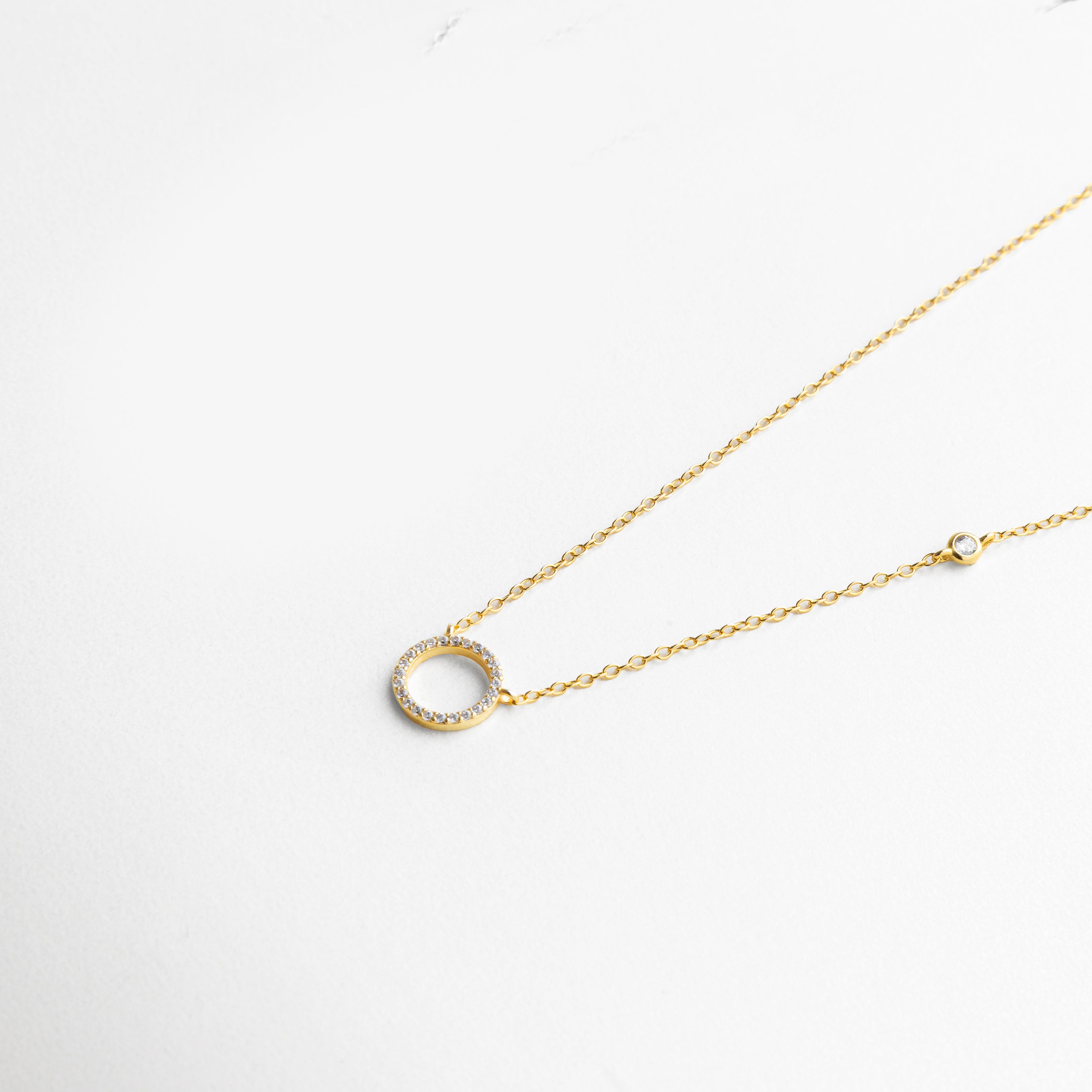 Primer plano del dije y la cadena bañada en oro 18K, donde las zirconias capturan la luz y realzan el acabado pulido con un destello refinado