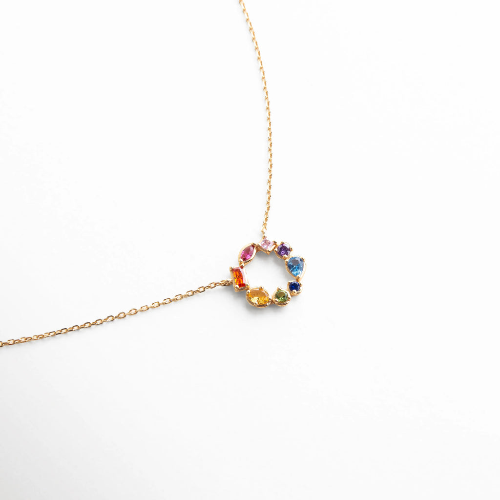 Collar dorado con dije circular adornado con piedras multicolor, diseño delicado y moderno que resalta por su brillo y color.