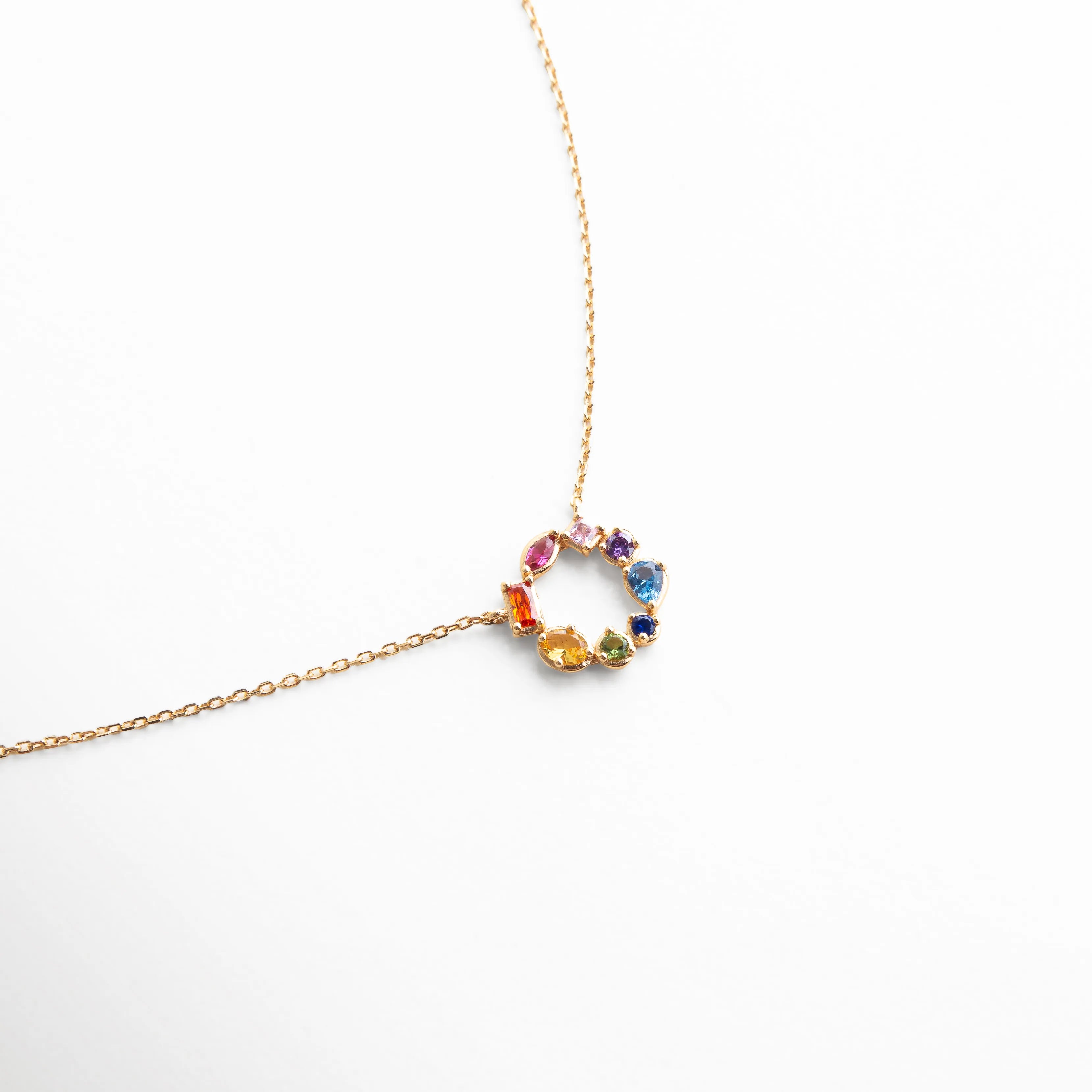 Collar dorado con dije circular adornado con piedras multicolor, diseño delicado y moderno que resalta por su brillo y color.