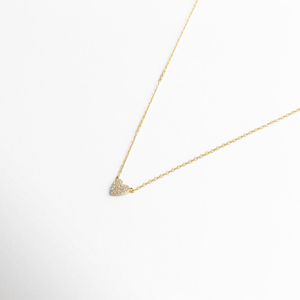 Detalle del dije de corazón con incrustaciones de zirconias, brillo sutil y diseño discreto que aporta un toque sofisticado y romántico, joyería fina para un estilo contemporáneo