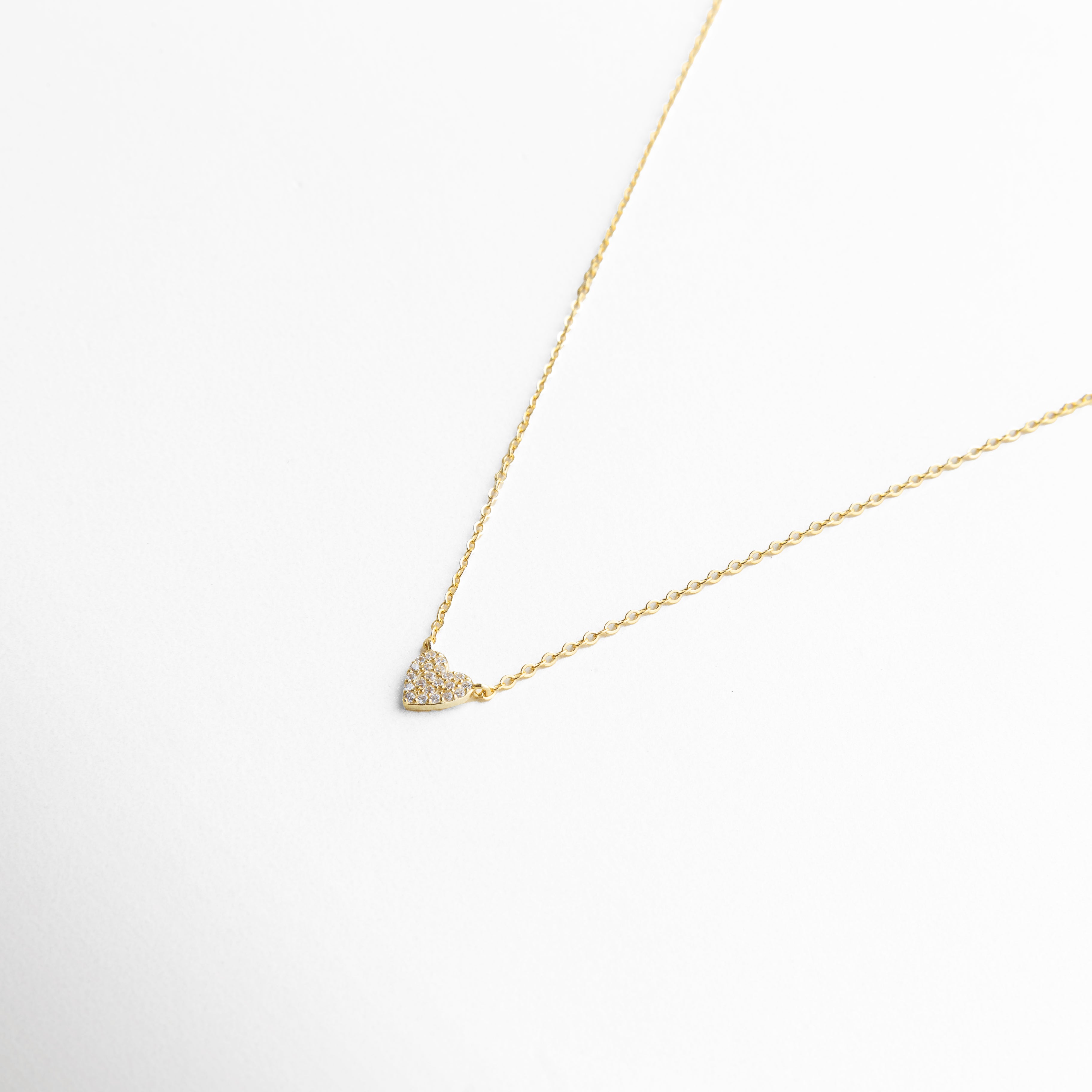 Detalle del dije de corazón con incrustaciones de zirconias, brillo sutil y diseño discreto que aporta un toque sofisticado y romántico, joyería fina para un estilo contemporáneo