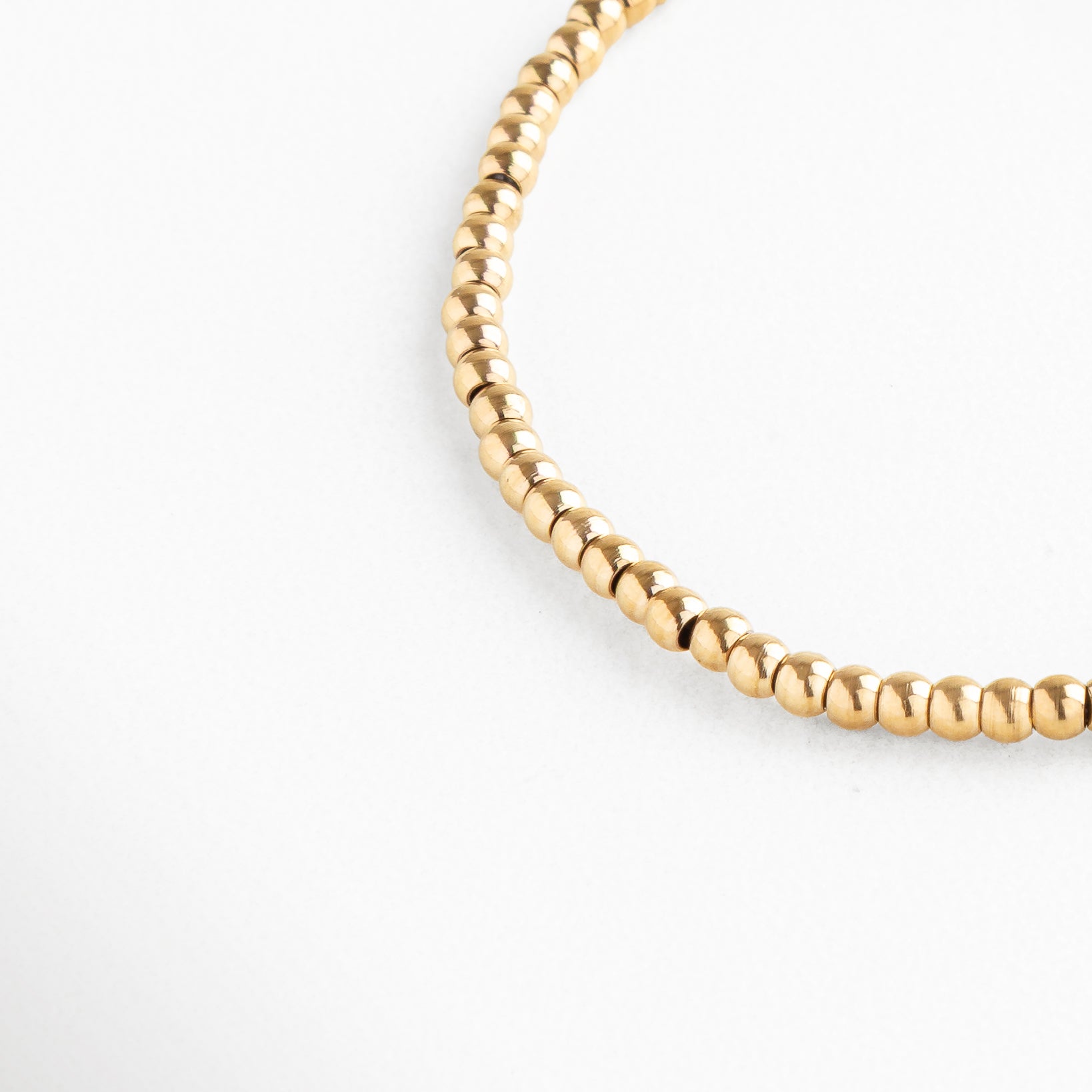 Detalle de pulsera dorada de cuentas redondas con acabado brillante, Pulsera dorada minimalista, detalle de cuentas metálicas pulidas.