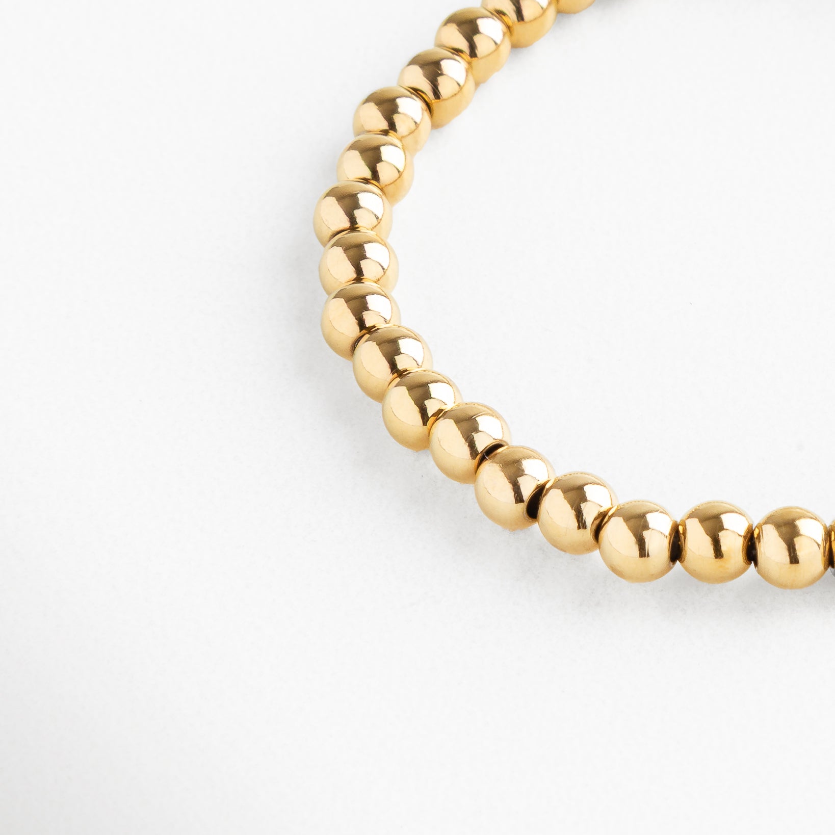 Detalle de pulsera dorada de cuentas medianas con acabado brillante, Pulsera dorada moderna, cuentas metálicas medianas pulidas.