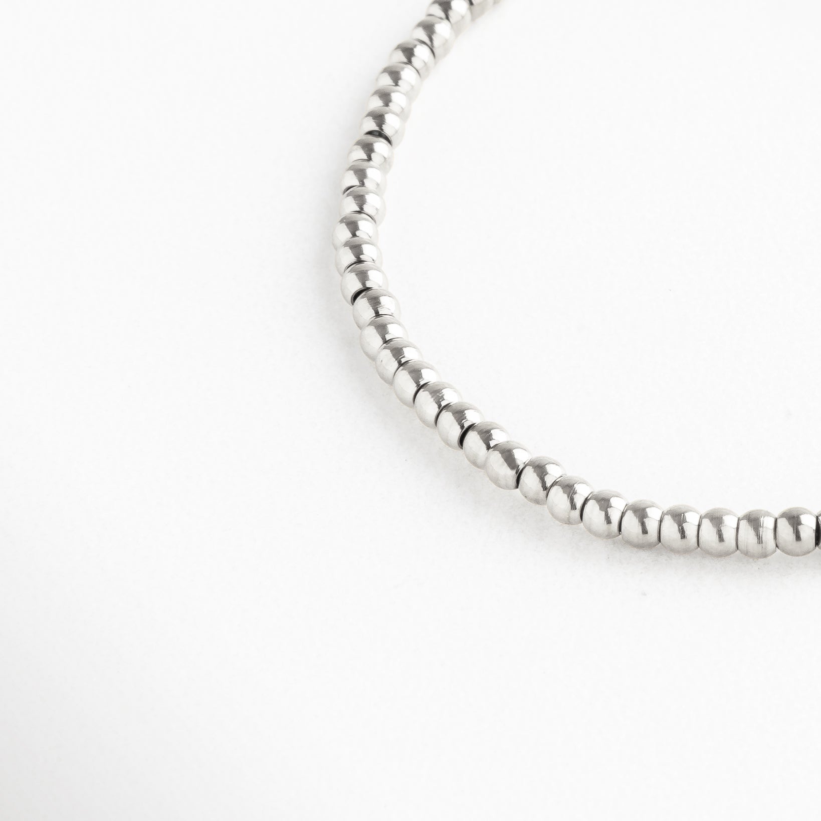Detalle en primer plano de pulsera plateada con cuentas redondas, acabado pulido y reflejante, diseño minimalista que resalta por su brillo sutil y sofisticado, perfecta para combinar con otros accesorios o charms