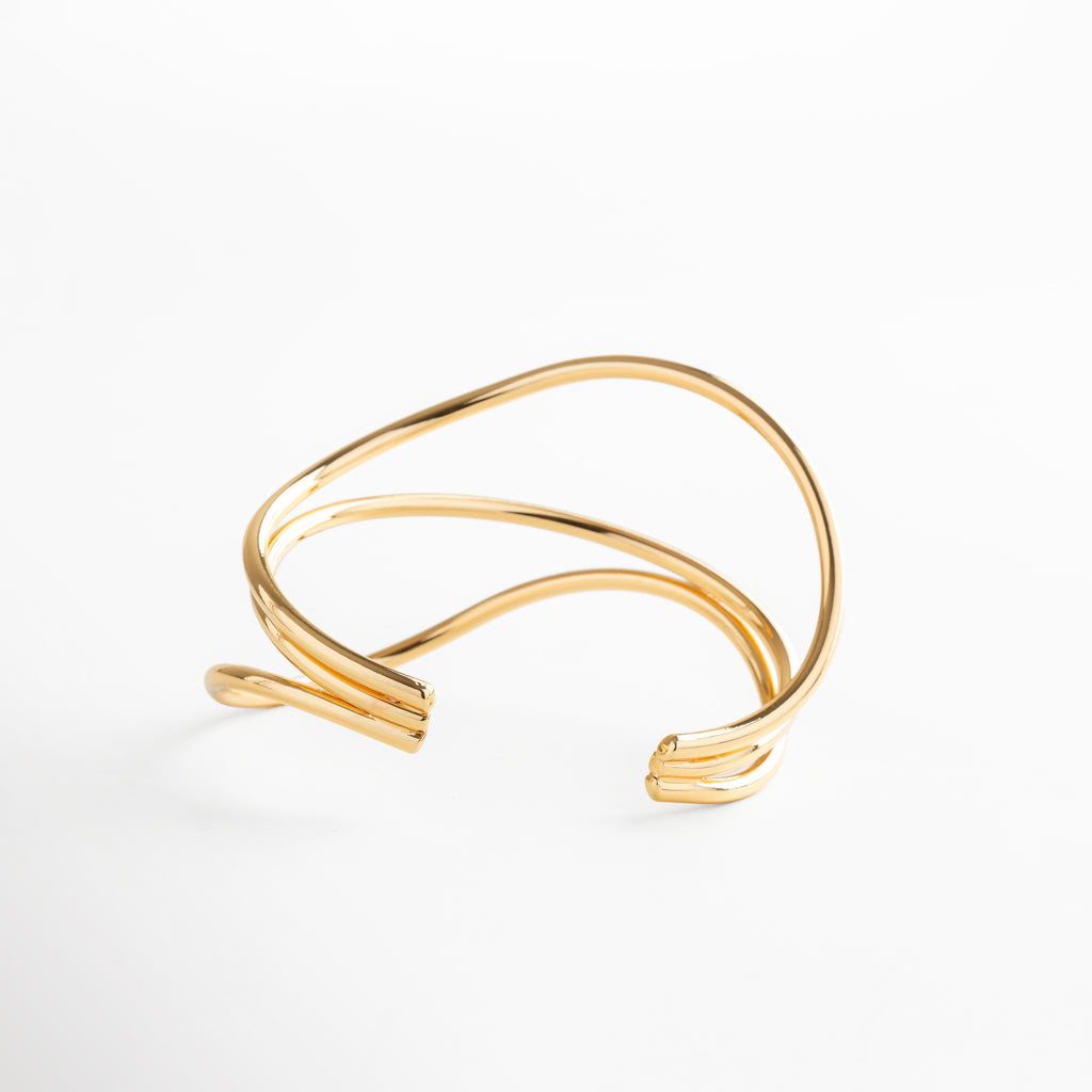 Pulsera dorada abierta con diseño entrecruzado y acabado brillante, joya escultural de oro 24K, sofisticada y ligera para destacar con estilo.
