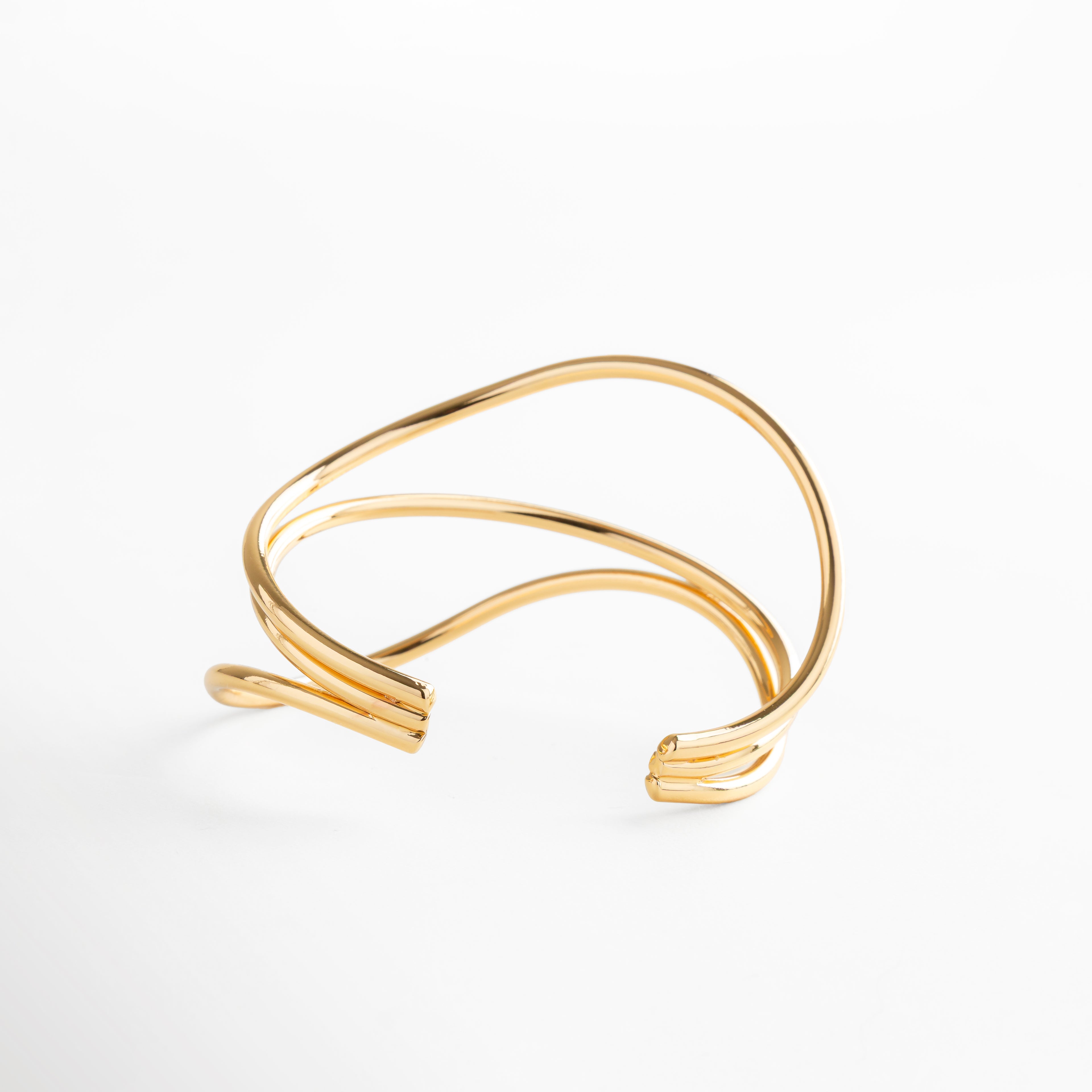 Pulsera dorada abierta con diseño entrecruzado y acabado brillante, joya escultural de oro 24K, sofisticada y ligera para destacar con estilo.