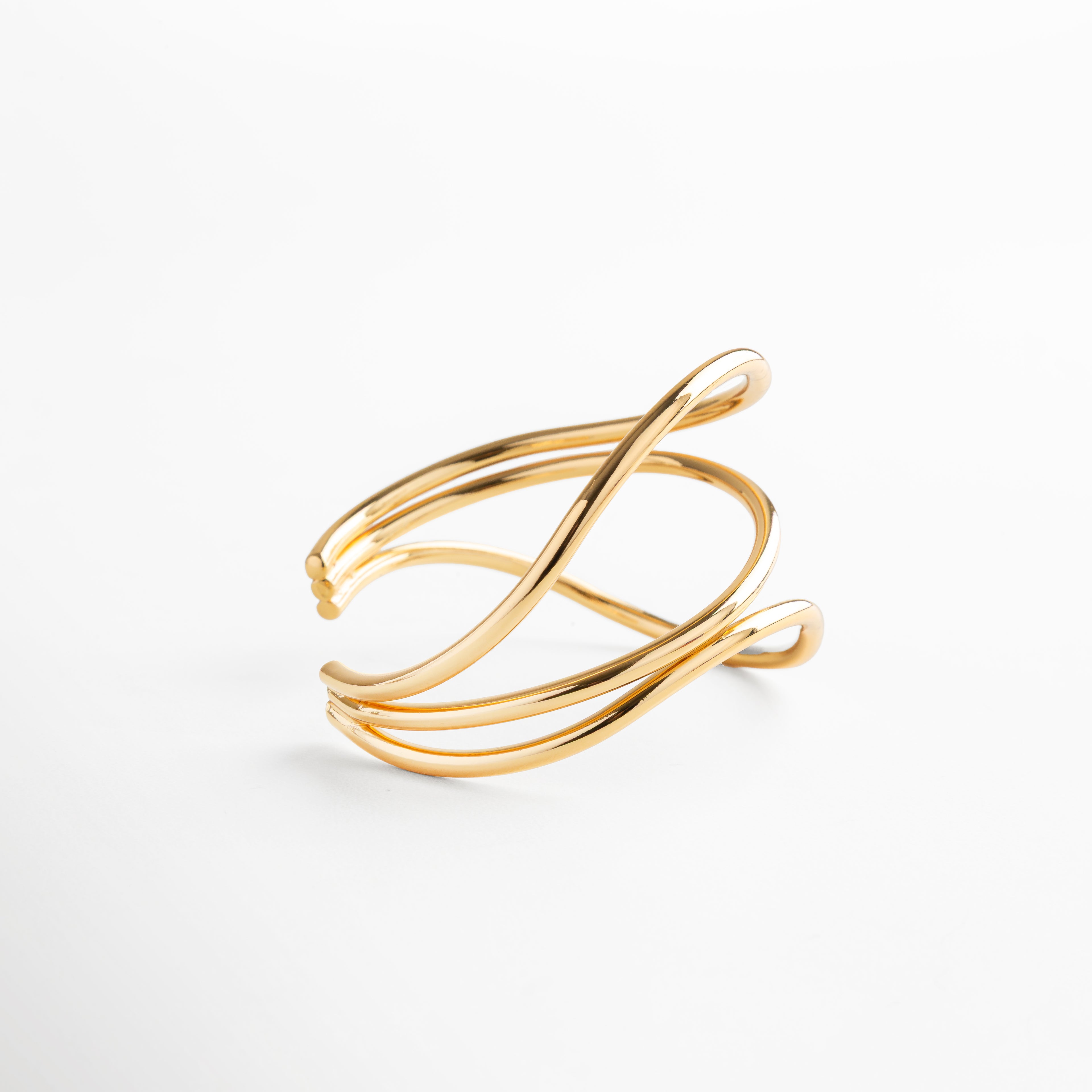 Pulsera dorada con forma escultórica y líneas curvas, acabado espejo en oro 24K, accesorio atemporal que equilibra movimiento y elegancia.