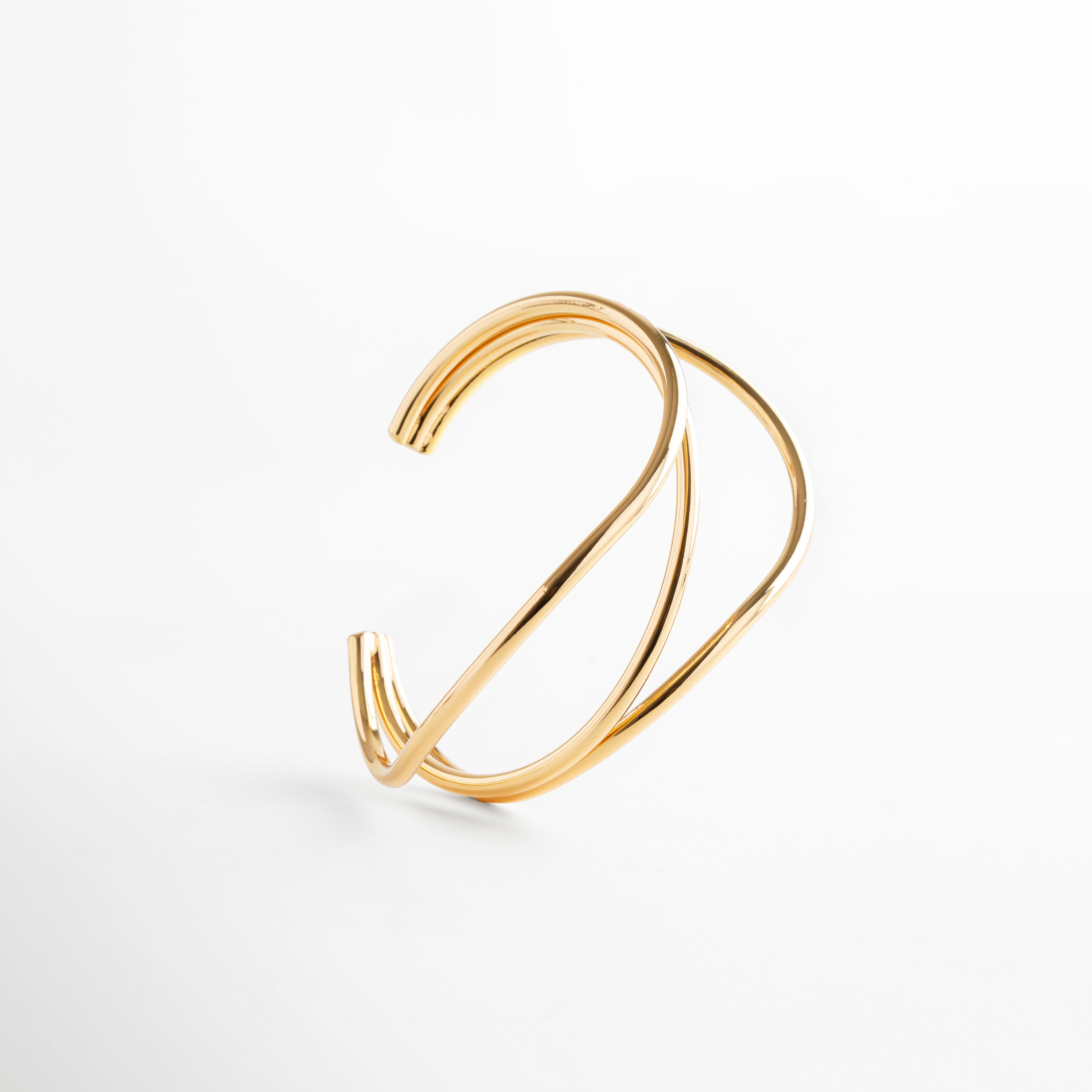 Pulsera dorada escultural con diseño fluido y entrelazado, latón con recubrimiento en acero inoxidable y baño en oro 24K, joya moderna y sofisticada.
