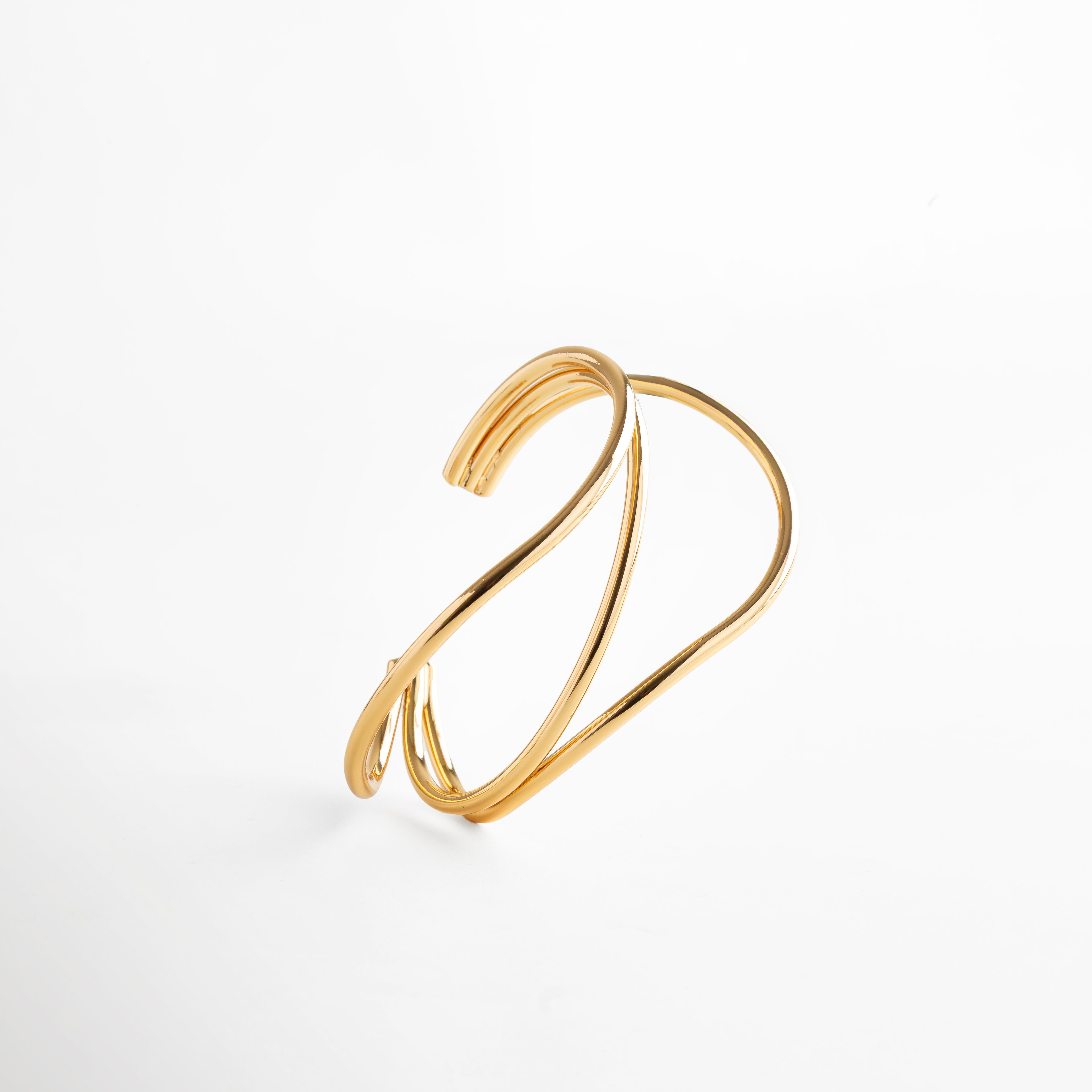 Brazalete fluido en dorado con estructura doble, diseño elegante en latón con recubrimiento en acero inoxidable y baño en oro 24K, complemento moderno y versátil.