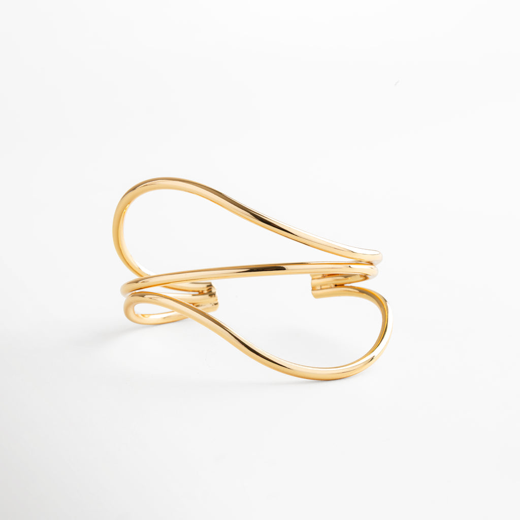 Brazalete dorado con silueta orgánica y curvas elegantes, pieza minimalista en oro 24K sobre latón, ideal para looks modernos y atemporales.