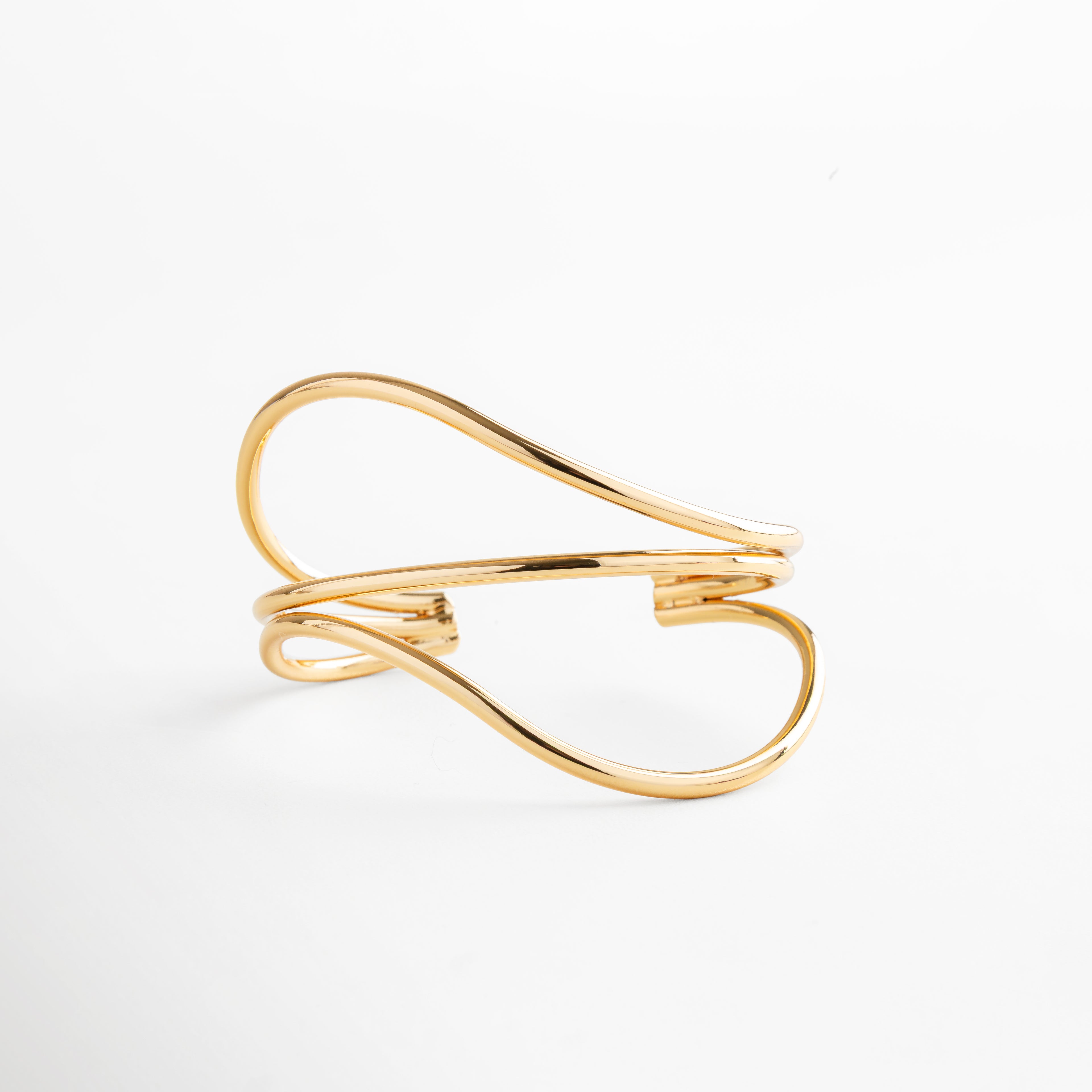Brazalete dorado con silueta orgánica y curvas elegantes, pieza minimalista en oro 24K sobre latón, ideal para looks modernos y atemporales.