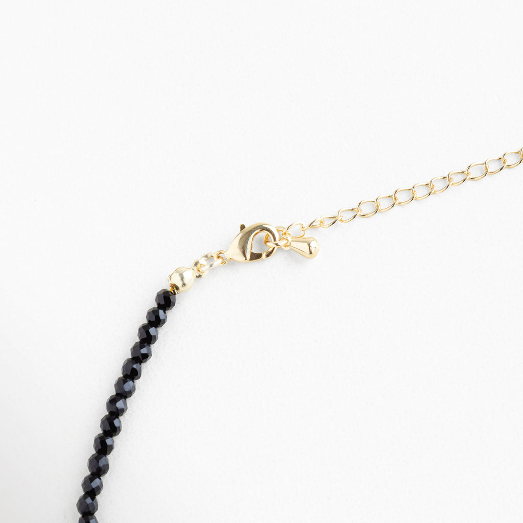 Detalle de broche dorado con extensión ajustable, collar de cuentas negras y cristales sintéticos, acabado en oro 18K para ajuste cómodo y seguro.
