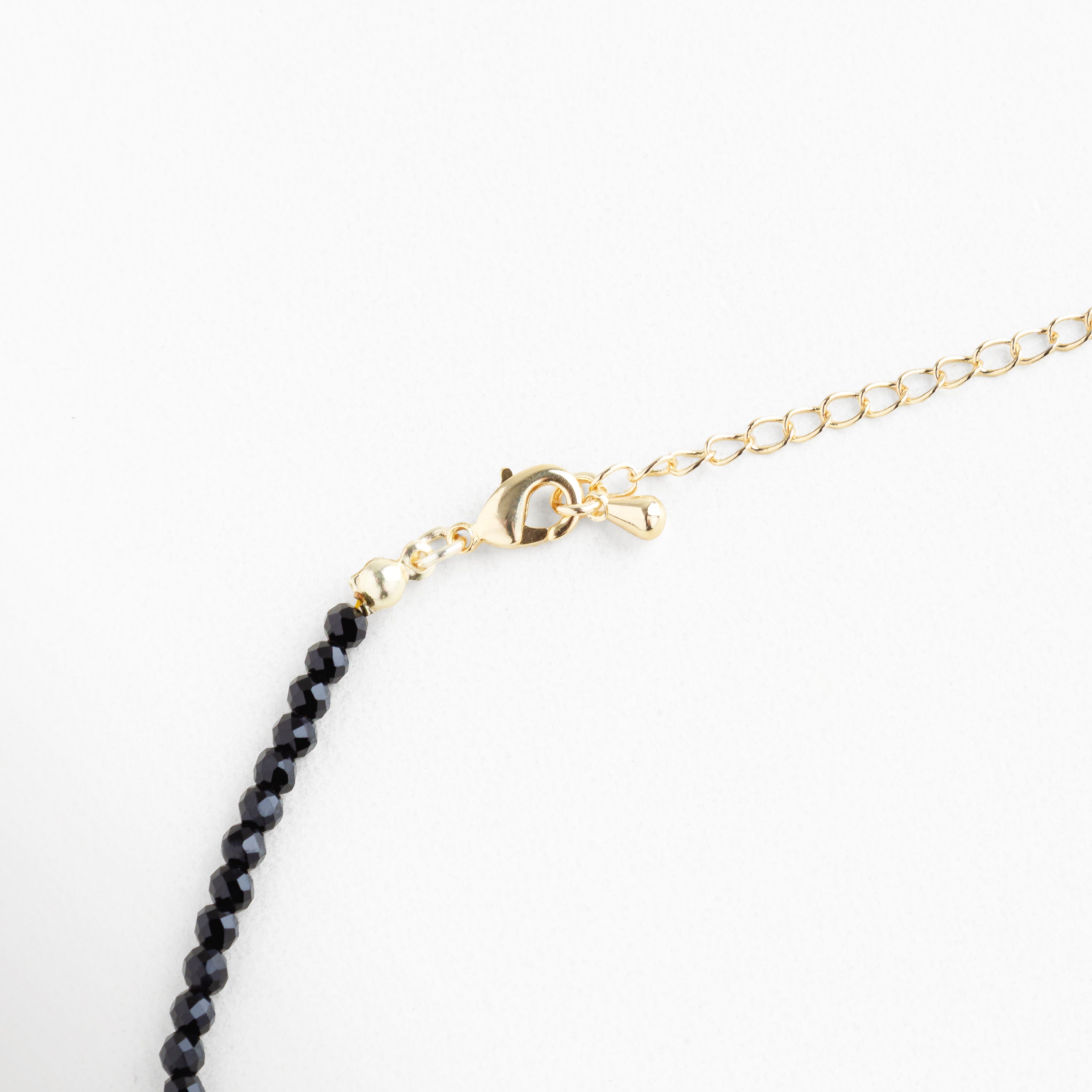 Detalle de broche dorado con extensión ajustable, collar de cuentas negras y cristales sintéticos, acabado en oro 18K para ajuste cómodo y seguro.