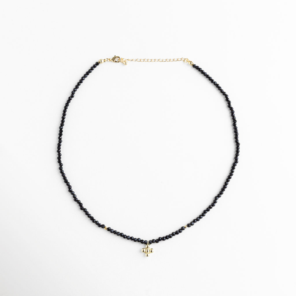 Collar corto de cuentas negras con dije dorado, cristales sintéticos y baño en oro 18K, accesorio versátil para looks casuales y sofisticados.