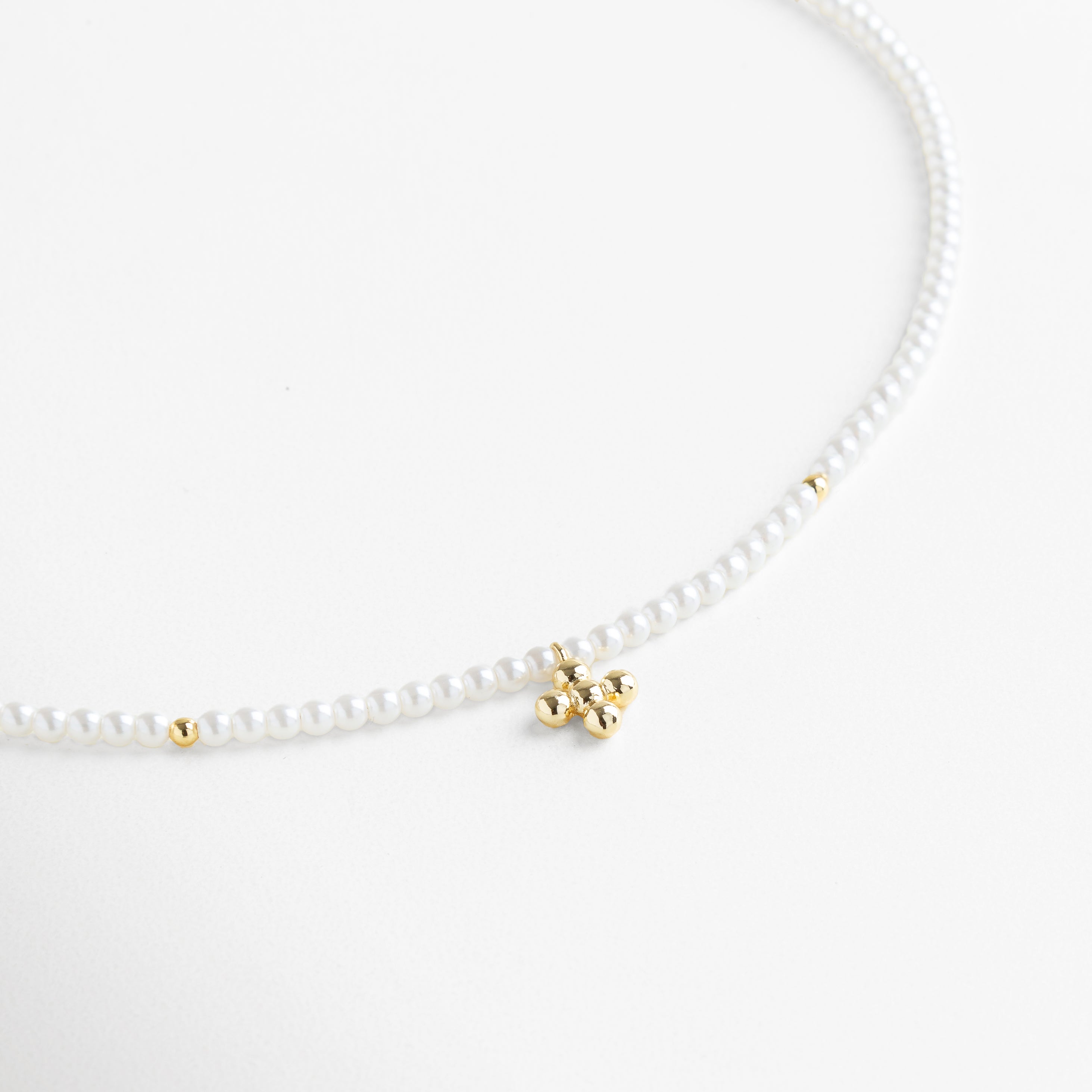Collar Perlina visto de frente, con perlas pequeñas unidas y un dije central en forma de cruz dorada. Vista frontal del collar de perlas sintéticas con diseño delicado y cruz dorada como punto focal. Collar clásico de perlas blancas con detalle central dorado visto desde el frente sobre fondo neutro. Primer plano frontal del Collar Perlina, resaltando su diseño femenino y armonioso. Collar de perlas sintéticas con dije de cruz en chapa de oro, ideal para un look elegante y atemporal.