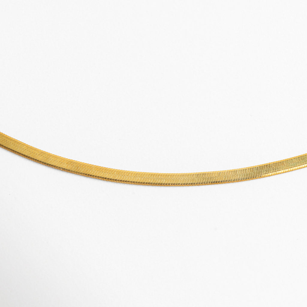 Detalle del acabado planchado del Collar Pressed Golden Aída dorado, mostrando el brillo uniforme de su superficie. Close-up de la cadena dorada con textura lisa y delgada, resaltando su elegancia discreta. Zoom al collar dorado con acabado planchado, con eslabones planos y estructura pulida. Detalle cercano del collar de plata 925 enchapado en oro, con diseño minimalista. Primer plano de la textura planchada del Collar Aída, capturando su efecto espejo y estilo moderno.