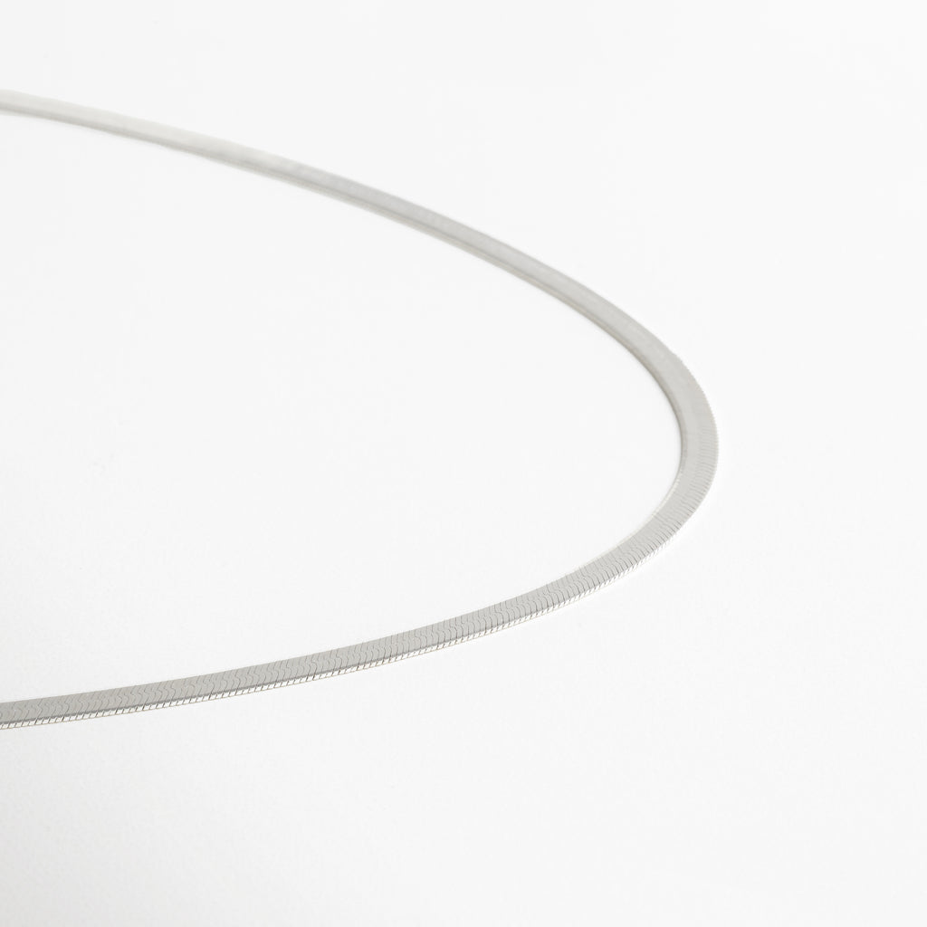 Collar Pressed Silver Aída visto de perfil, mostrando su grosor delgado y caída uniforme. Vista lateral del collar plateado, resaltando su acabado planchado y líneas limpias. Perfil del collar minimalista en plata, diseño elegante y discreto. Detalle lateral del collar Pressed Silver Aída, mostrando su estructura ligera y pulida. Collar plateado visto desde un ángulo lateral, diseño versátil y acabado reflectivo.
