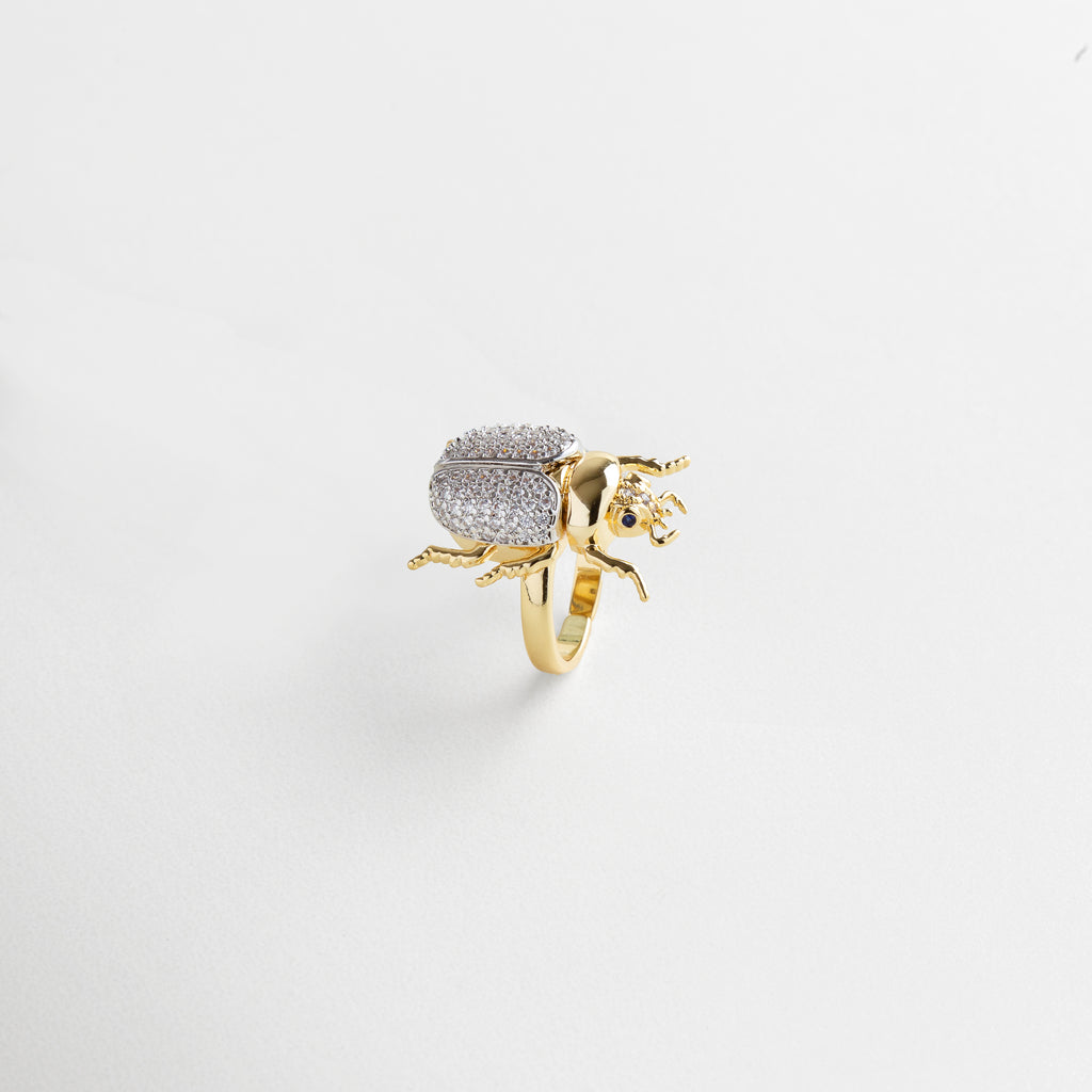 zirconias engastadas en el escarabajo, acabado pulido espejo en oro 18K, detalle fino en patas y alas del escarabajo, textura uniforme y brillante, diseño delicado con carácter