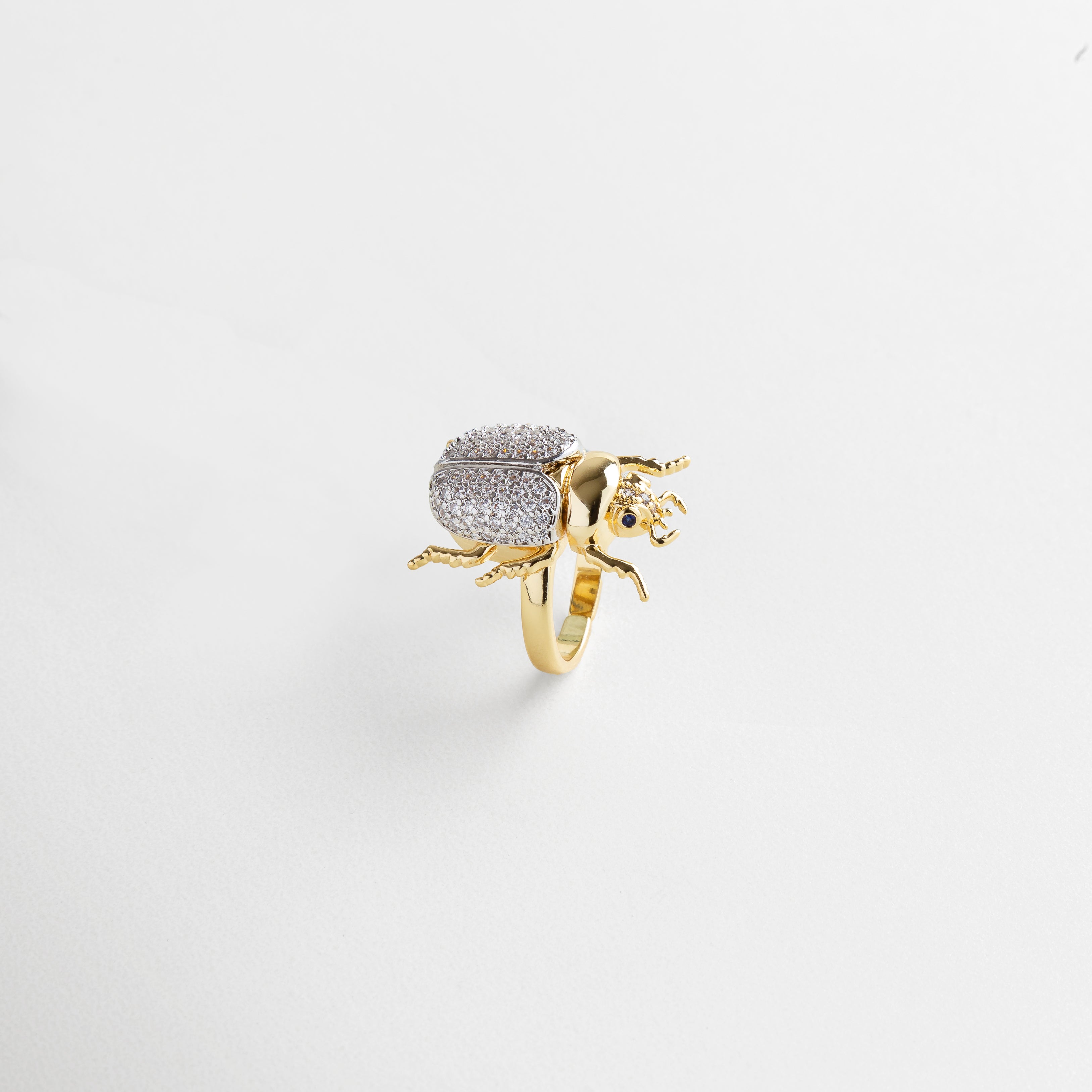 zirconias engastadas en el escarabajo, acabado pulido espejo en oro 18K, detalle fino en patas y alas del escarabajo, textura uniforme y brillante, diseño delicado con carácter