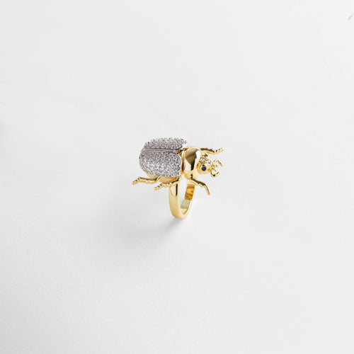 zirconias engastadas en el escarabajo, acabado pulido espejo en oro 18K, detalle fino en patas y alas del escarabajo, textura uniforme y brillante, diseño delicado con carácter