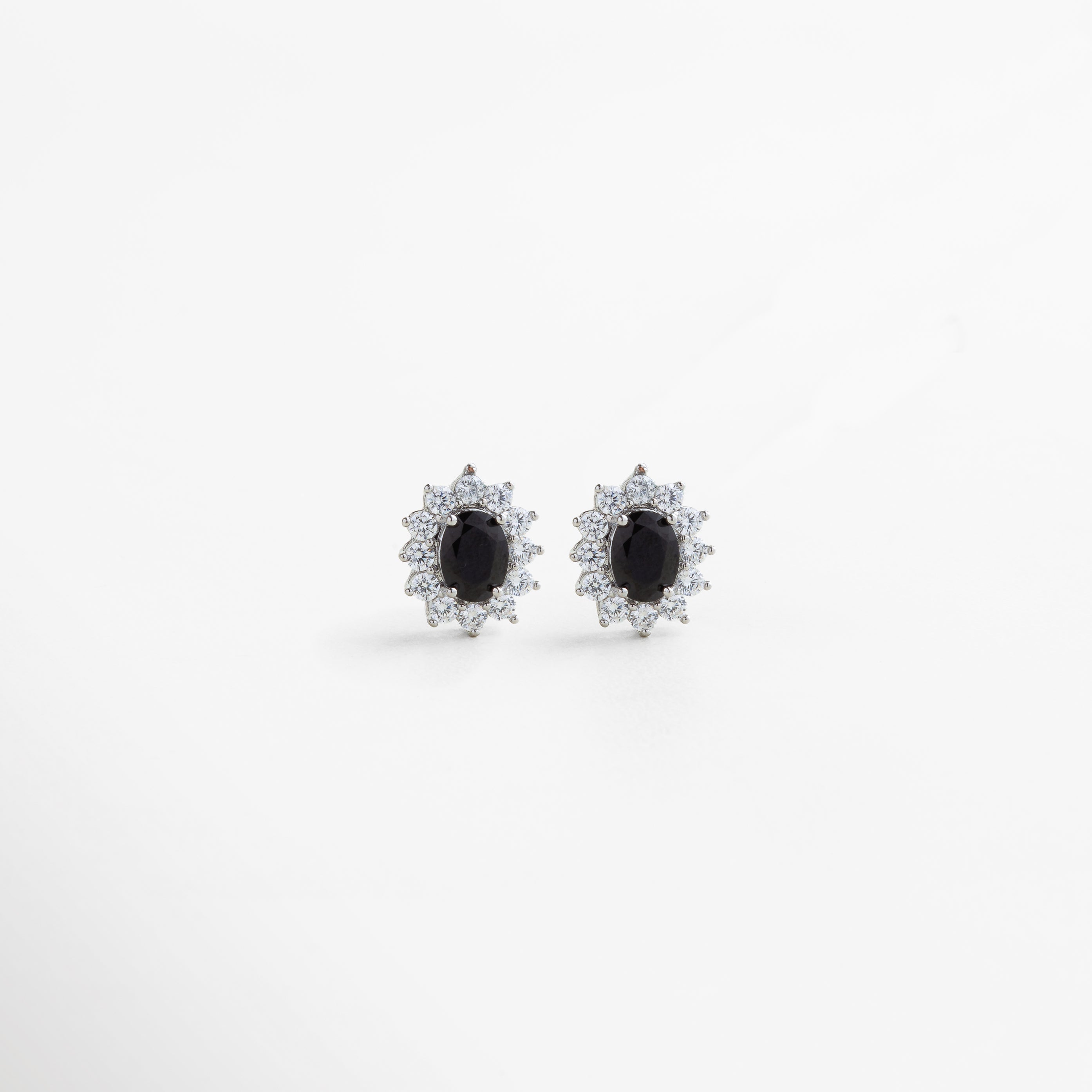 aretes plateados con centro de cristal negro, joya de cobre con baño de plata esterlina y zirconias, aretes elegantes con halo brillante y piedra central oscura, diseño sofisticado en plata con contraste negro, pendientes plateados con detalle central en cristal