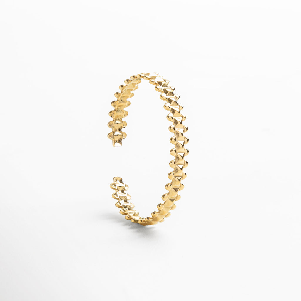 Primer plano del acabado dorado pulido que refleja luz, Detalle del recubrimiento en oro 18K con textura refinado, Diseño ajustable con estructura geométrica definida, Acabado suave que aporta un brillo cálido y sofisticado, Enfoque en las líneas limpias y ángulos delicados
