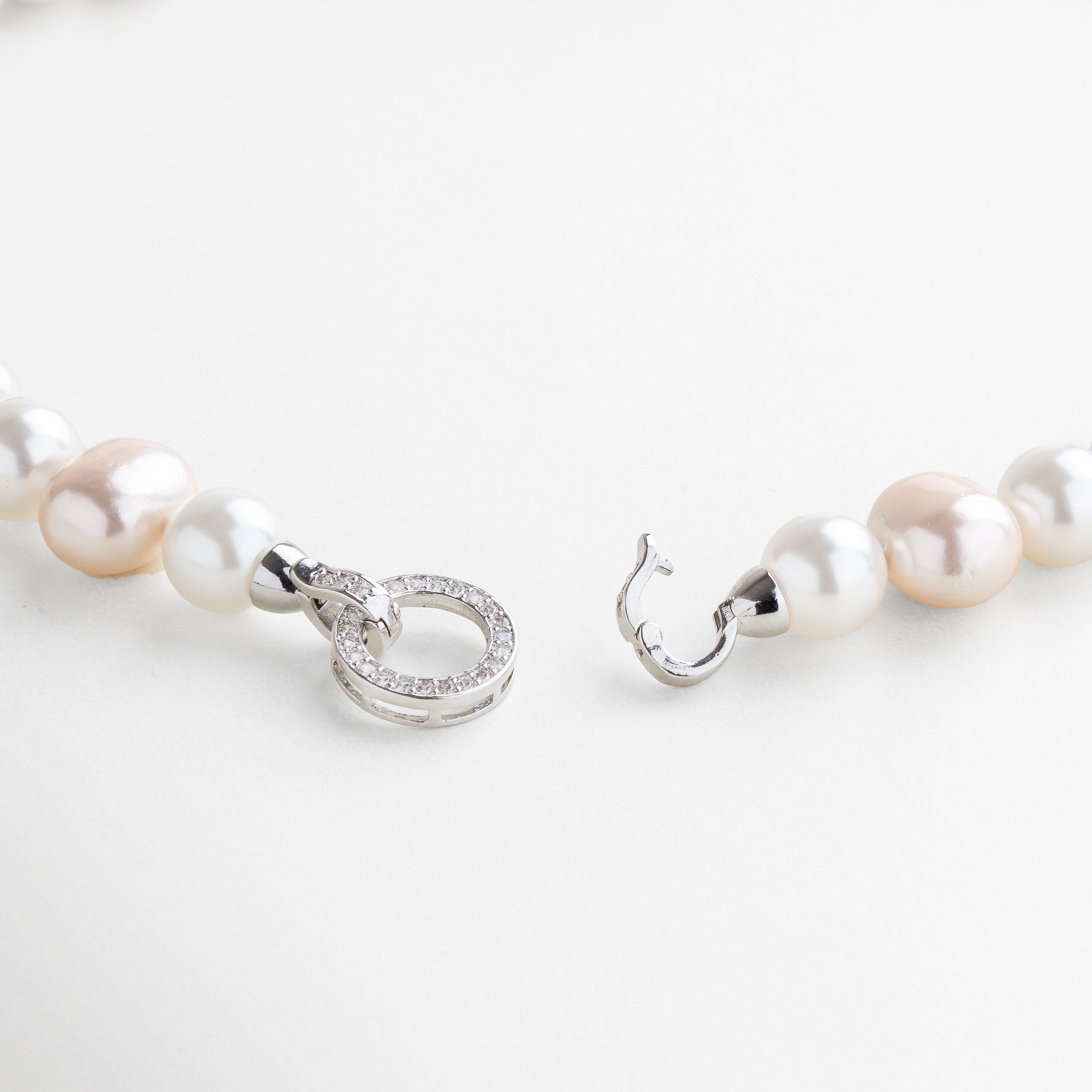 Detalle cercano del Collar Jolette White Pearl, con perlas blancas de superficie suave y acabado natural. Close-up del collar de conchas de agua dulce, mostrando la textura nacarada y la forma orgánica de cada perla. Zoom a las perlas blancas con recubrimiento de plata esterlina, resaltando su brillo sutil y elegante. Primer plano del diseño uniforme del collar de perlas, ideal para eventos formales o uso diario sofisticado. Detalle de las cuencas de concha natural, unidas en secuencia armon