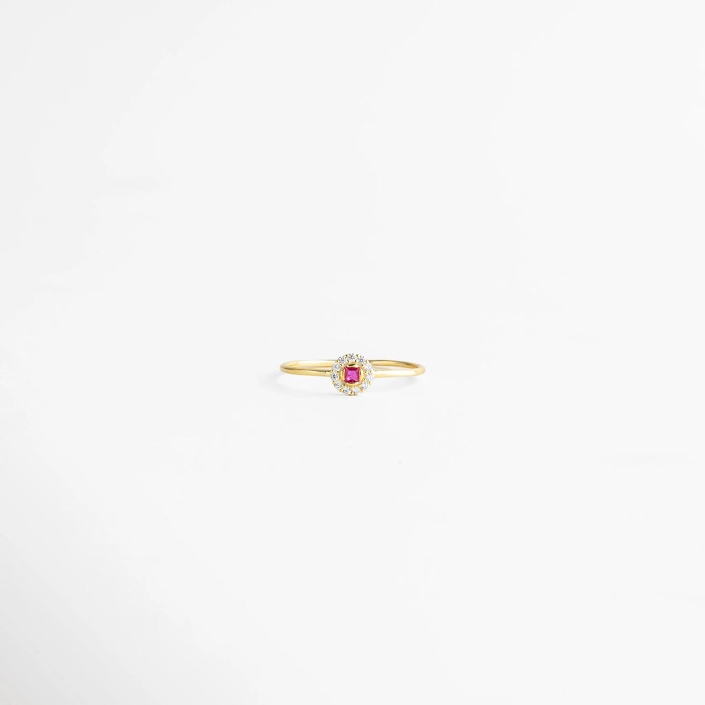 Anillo dorado con piedra central color fucsia en corte cuadrado, rodeada de destellos brillantes que realzan su elegancia.
