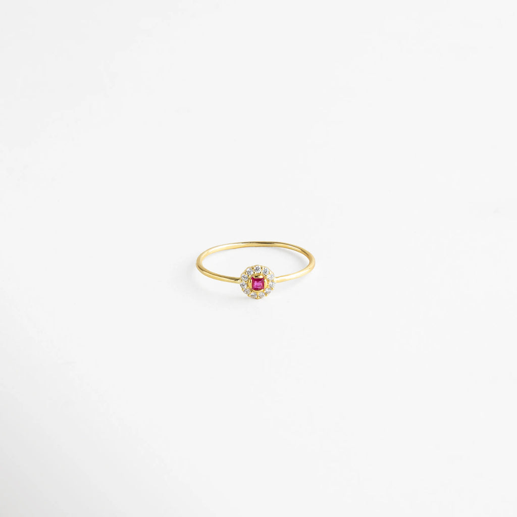 Anillo dorado con centro de piedra fucsia rodeada de cristales transparentes, un diseño delicado y femenino.